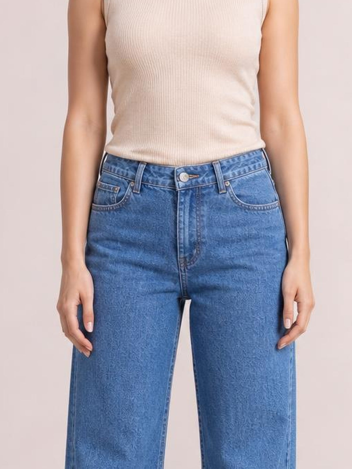 Model stands with hands at her sides wearing blue wide leg jeans with front pockets, belt loops, button closure, and a straight, relaxed silhouette.