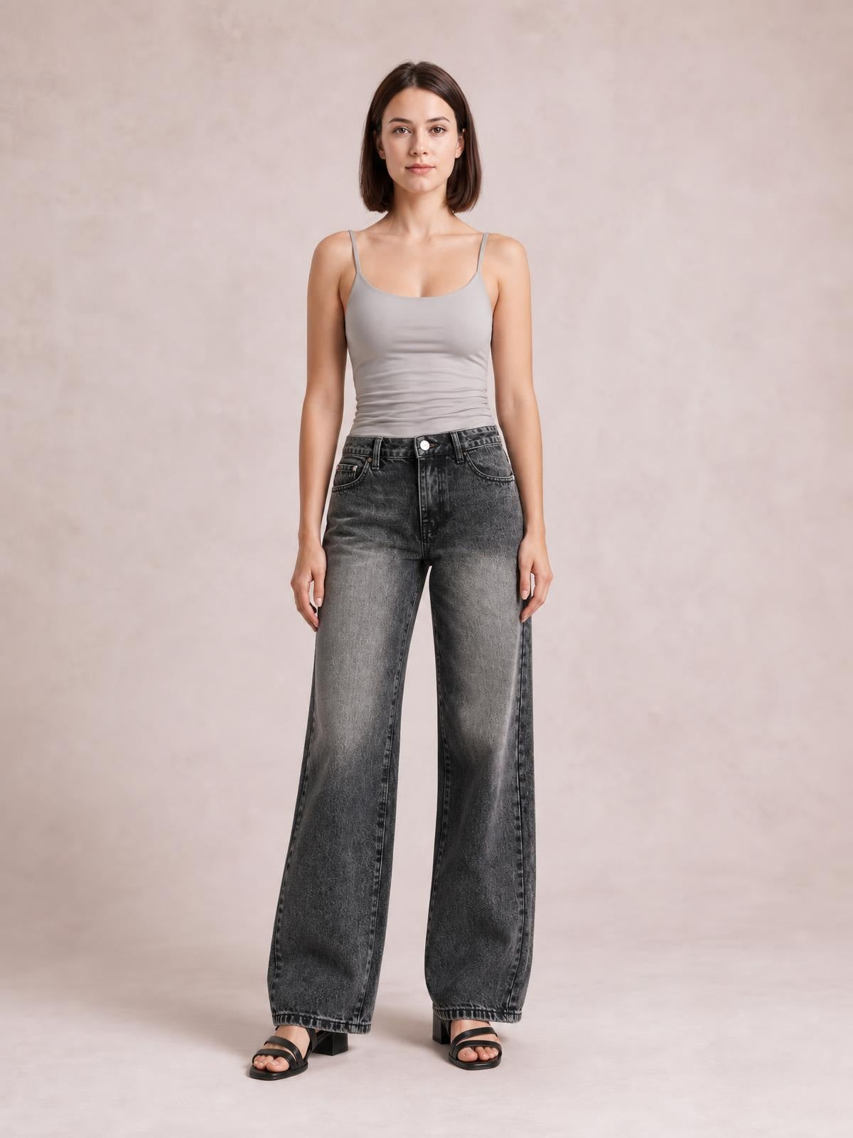 Model standing in dark gray wide-leg jeans with front pockets, belt loops, button closure, high waist, and relaxed full-length silhouette.