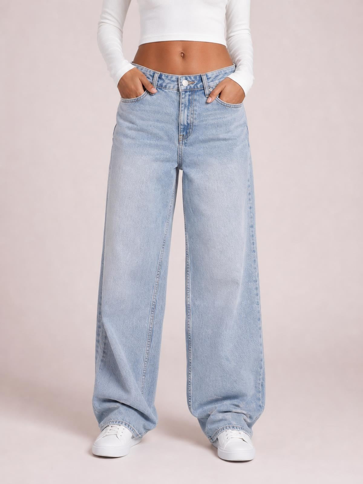 Model wearing light blue wide leg jeans with front pockets, a button closure, belt loops, and a relaxed full-length silhouette, standing with hands in pockets.