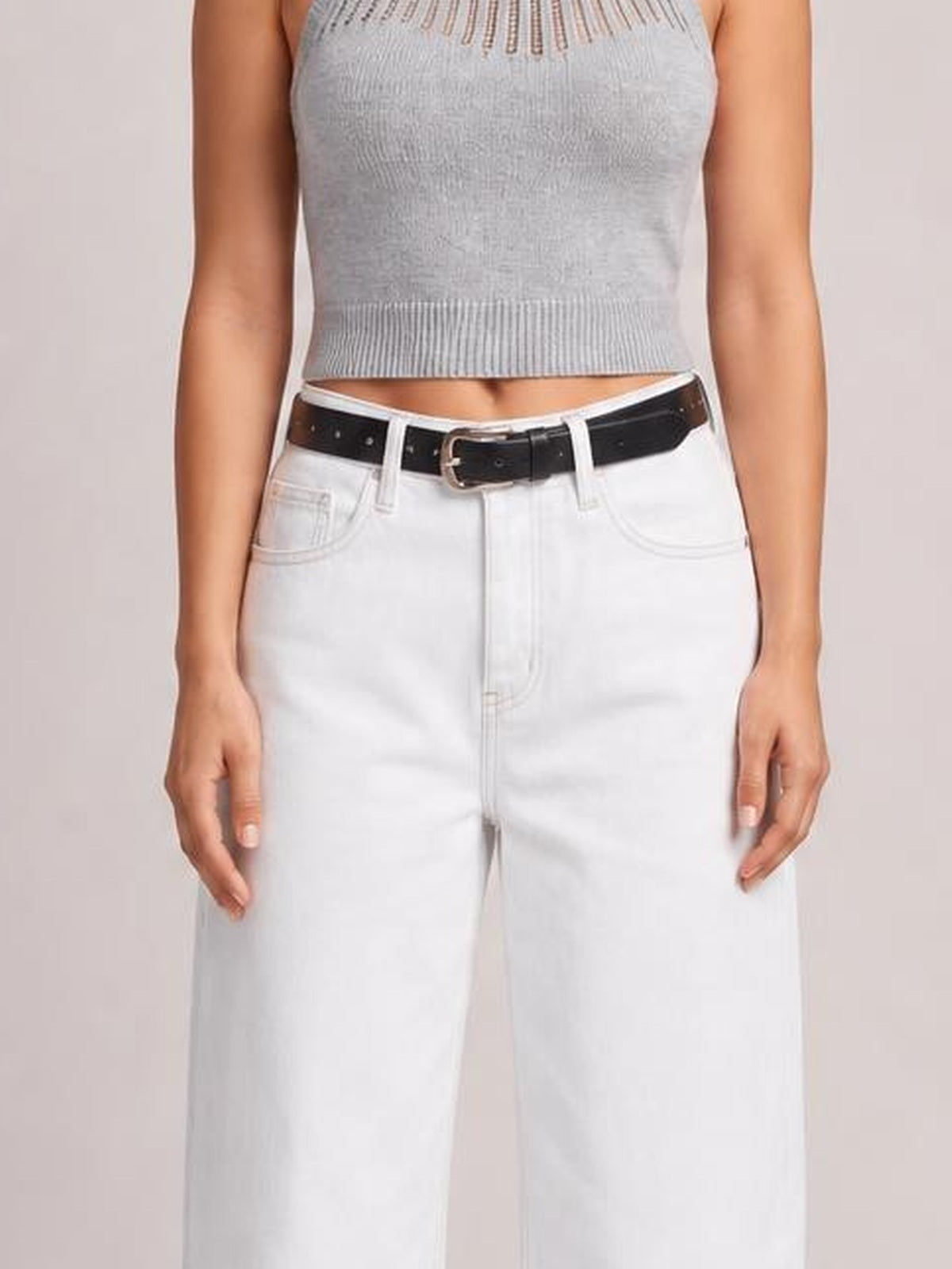 Model wears white wide leg jeans with a button fly, belt loops, and curved front pockets, shown from the waist down in a relaxed standing pose.