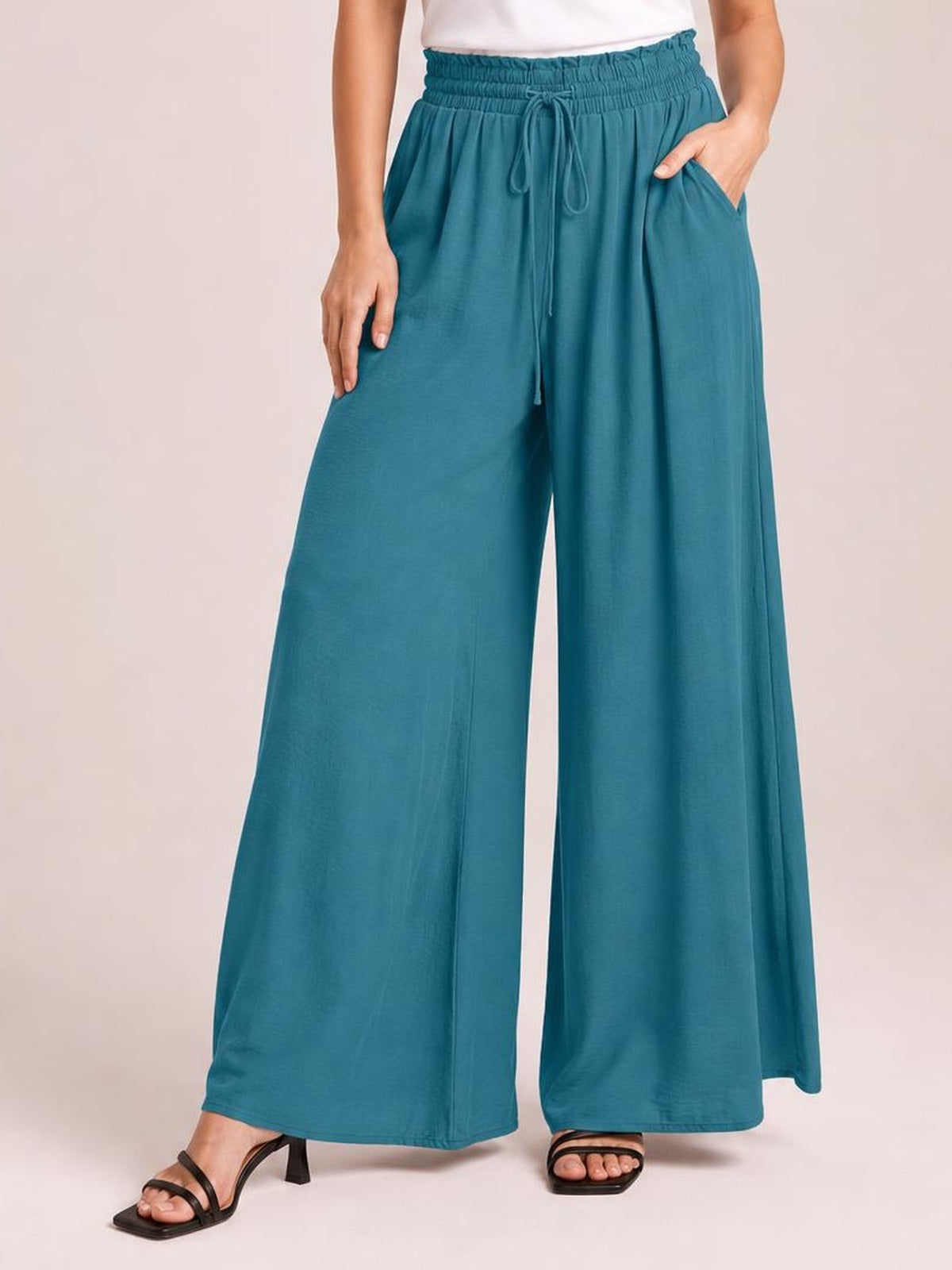 Model wearing teal wide leg pants with side pockets, a smocked elastic waistband, drawstring tie, and relaxed floor-length silhouette.