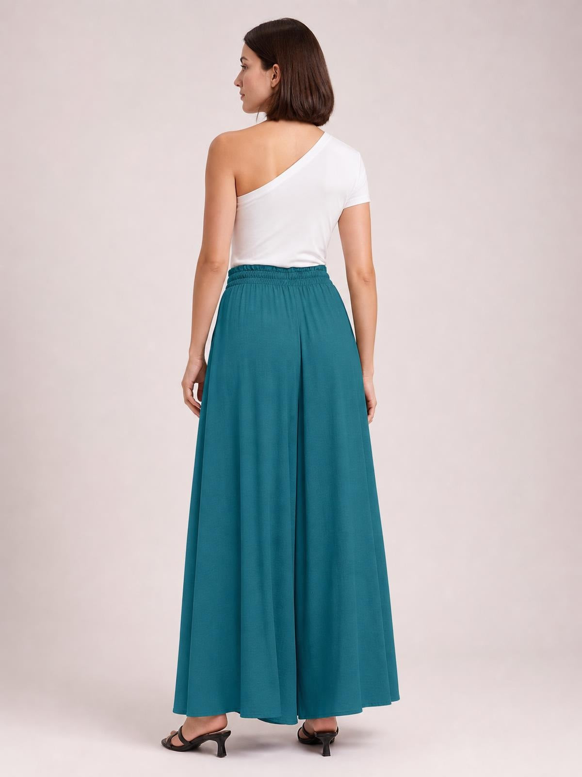 Model shown from the back wears teal wide-leg pants with a flowing silhouette, gathered elastic waistband, and practical side pockets.