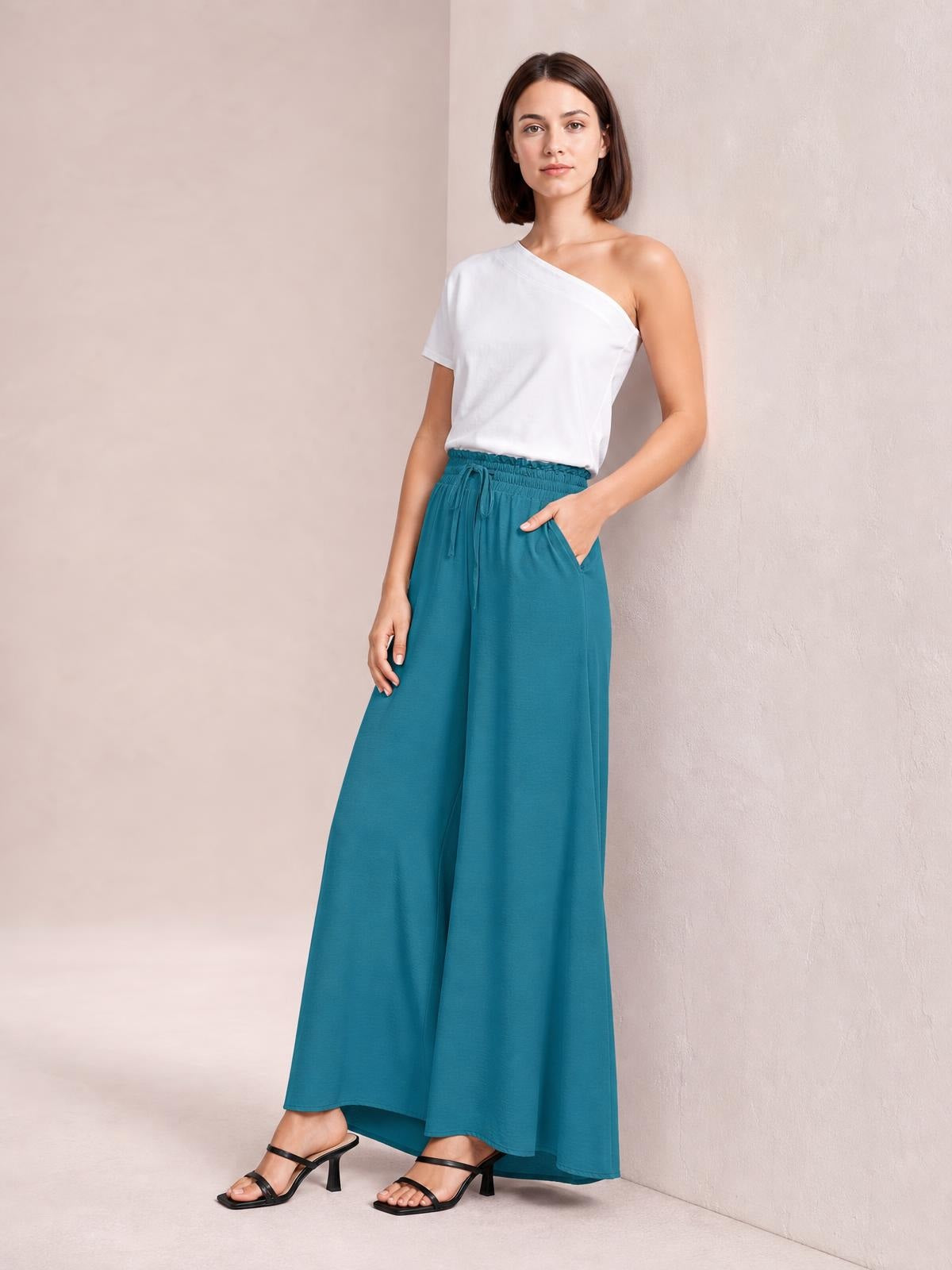 Model poses in teal wide leg pants with a drawstring waist, flowing floor-length silhouette, and visible side pockets.