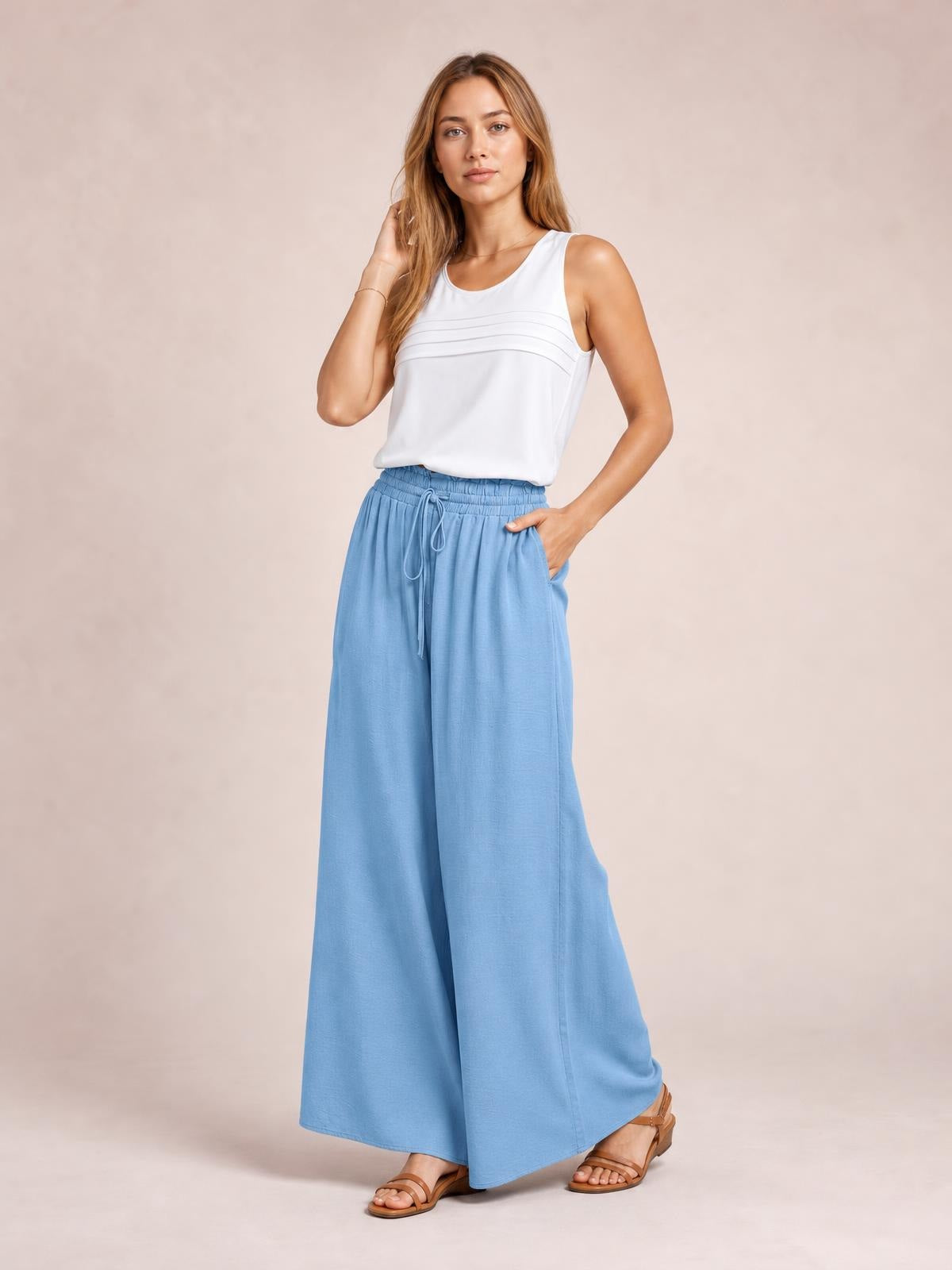 Model poses in light blue wide leg pants with an elastic drawstring waist and side pockets, styled with a white sleeveless top.