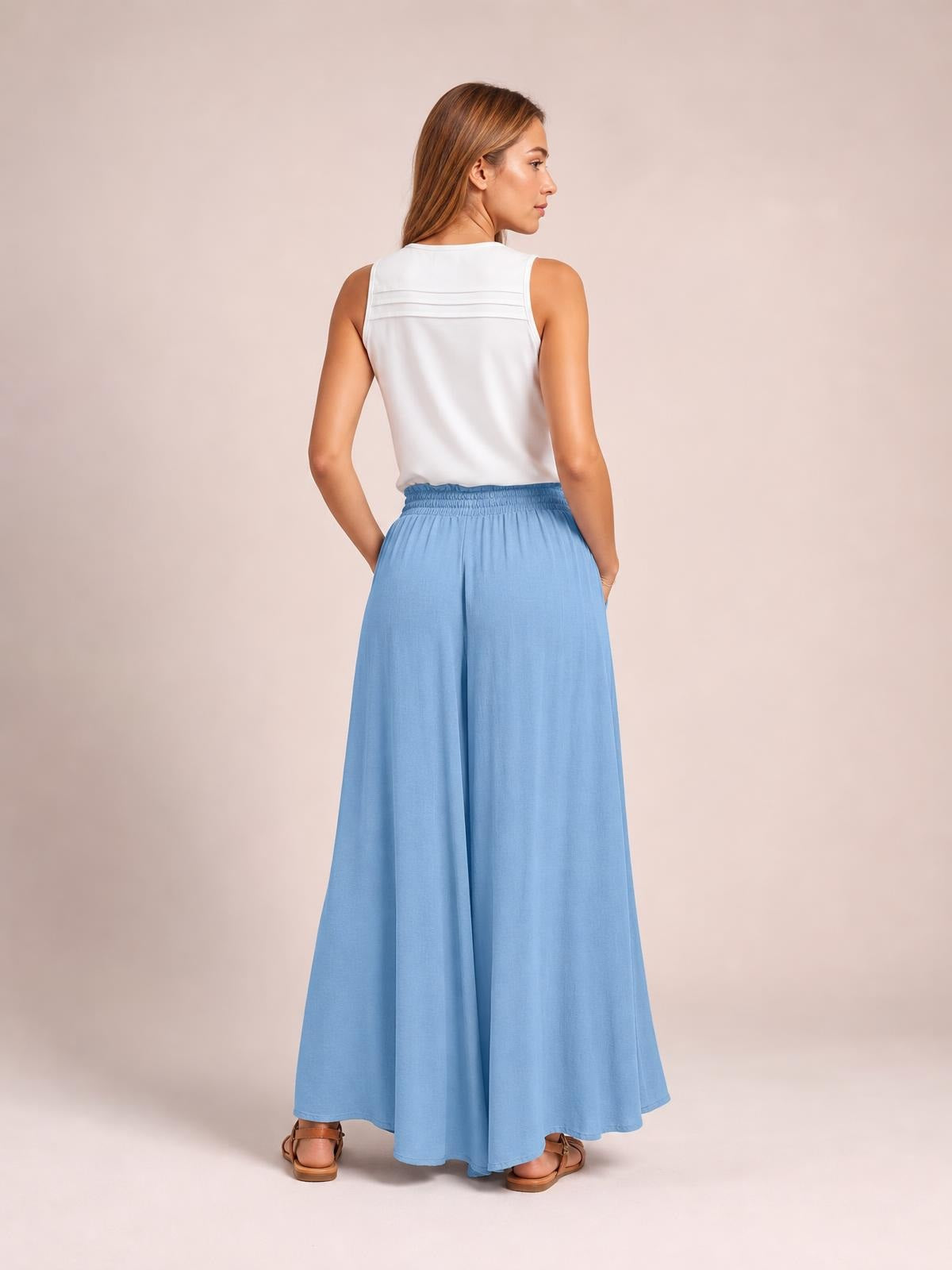 Model poses with hands in the pockets of light blue wide leg pants, featuring an elastic waistband and flowing full-length silhouette.
