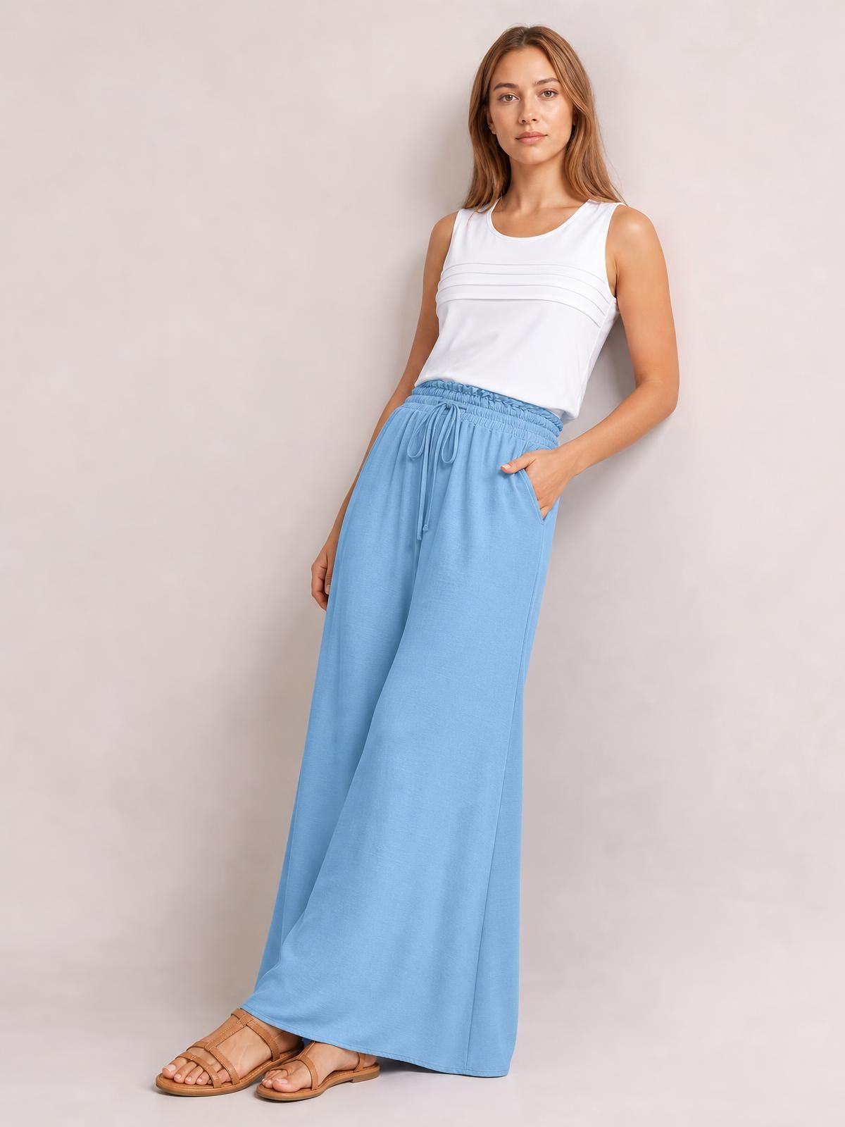 Model poses in light blue wide leg pants with a drawstring elastic waist and side pockets, styled with a white sleeveless top.