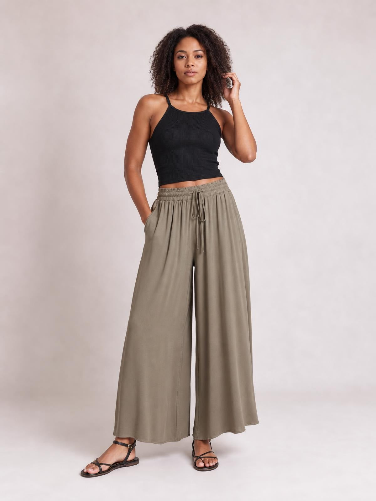 Model poses in taupe wide leg pants with side pockets, a stretchy gathered drawstring waist, and flowing full-length silhouette.