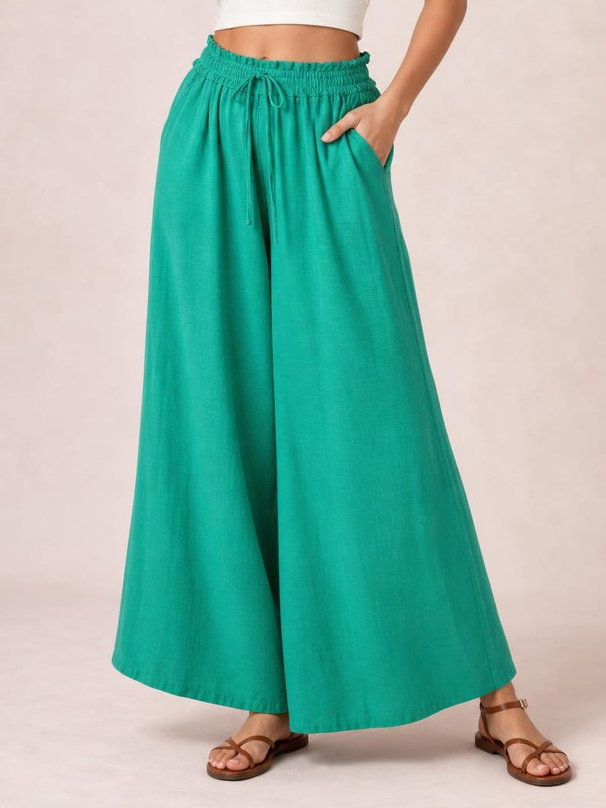 Model wears turquoise wide leg pants with an elastic drawstring waistband and side pockets, shown in a relaxed stance with one hand tucked into a pocket.