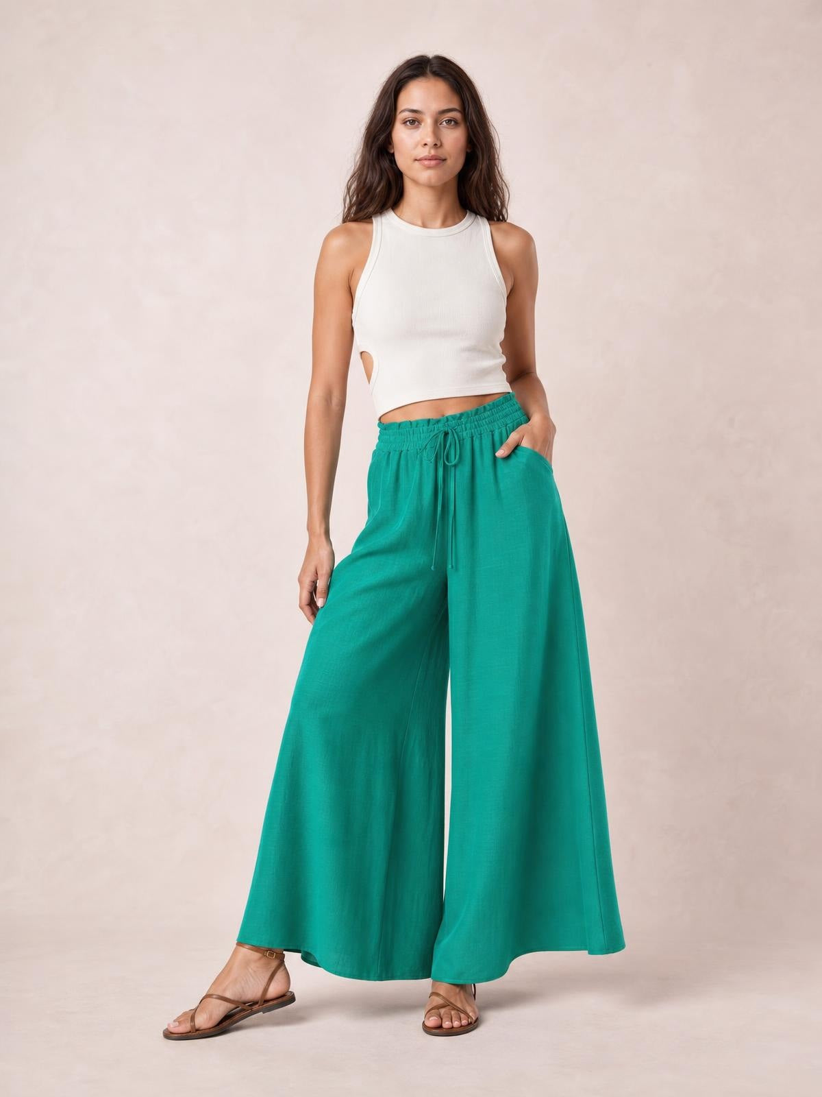 Model poses in vibrant teal wide leg pants with an elastic drawstring waist and visible side pockets, styled with a fitted white cropped tank.