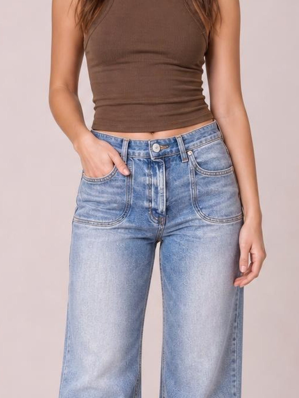 Model wearing light blue washed wide-leg jeans with a button fly, belt loops, contrast stitching, and large front pockets, one hand tucked into a pocket.
