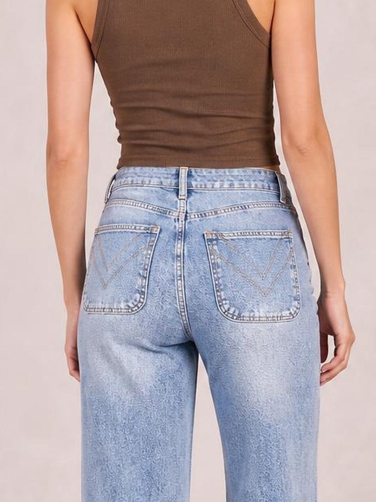 A model stands facing away in light blue washed wide-leg jeans with a structured waistband, belt loops, contrast stitching, and two back pockets.