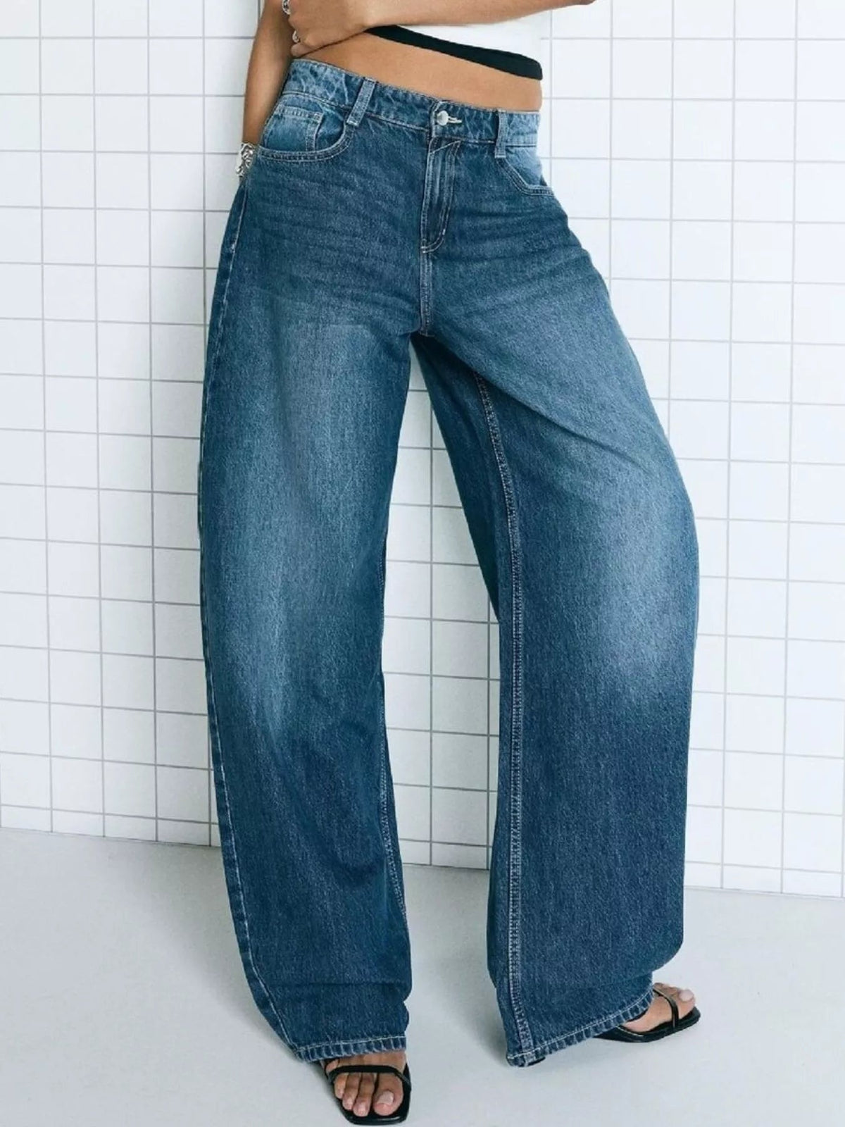 Model wearing blue washed wide-leg jeans with a button closure, belt loops, front pockets, and straight full-length legs, standing with one hip tilted.