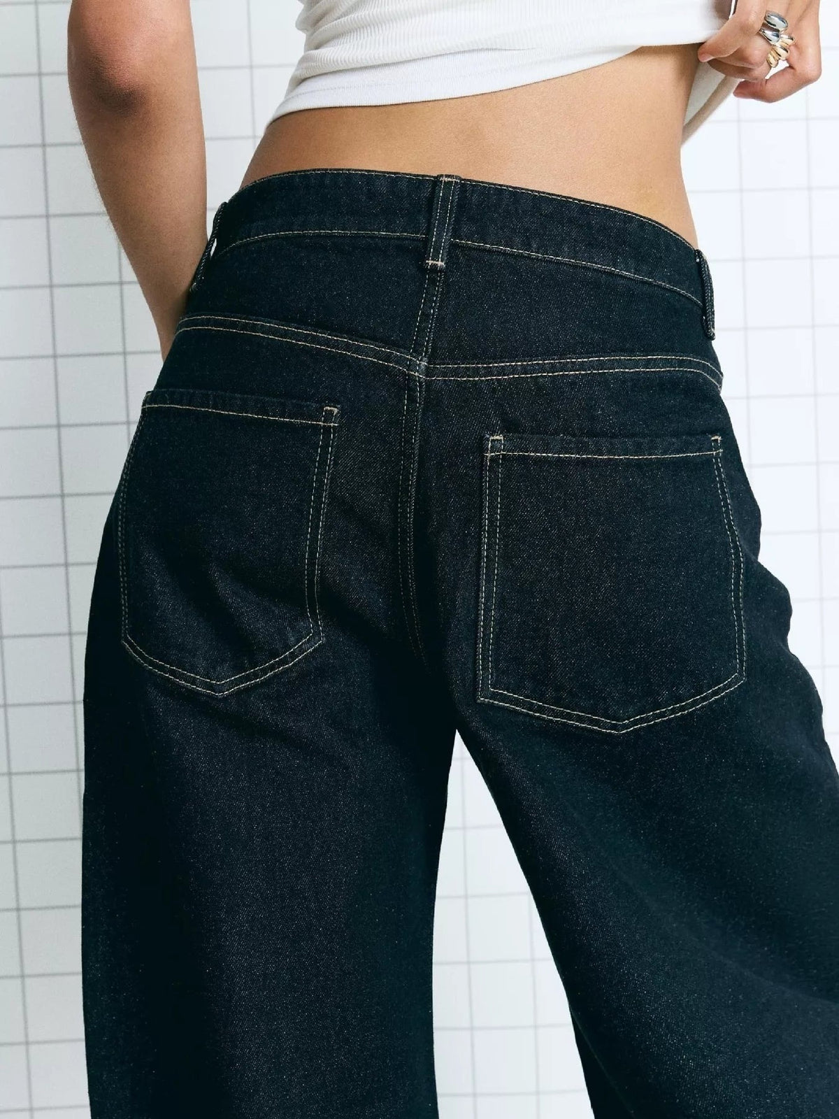 Close-up of a model wearing dark washed wide-leg jeans with a structured waistband, contrast stitching, belt loops, and two back patch pockets.
