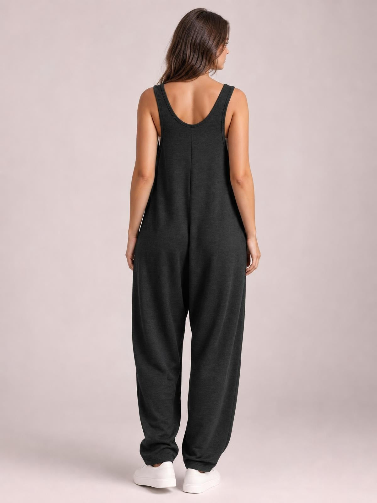 A model poses from the back in a black wide-strap jumpsuit with a scoop back, relaxed wide-leg silhouette, and practical pockets.