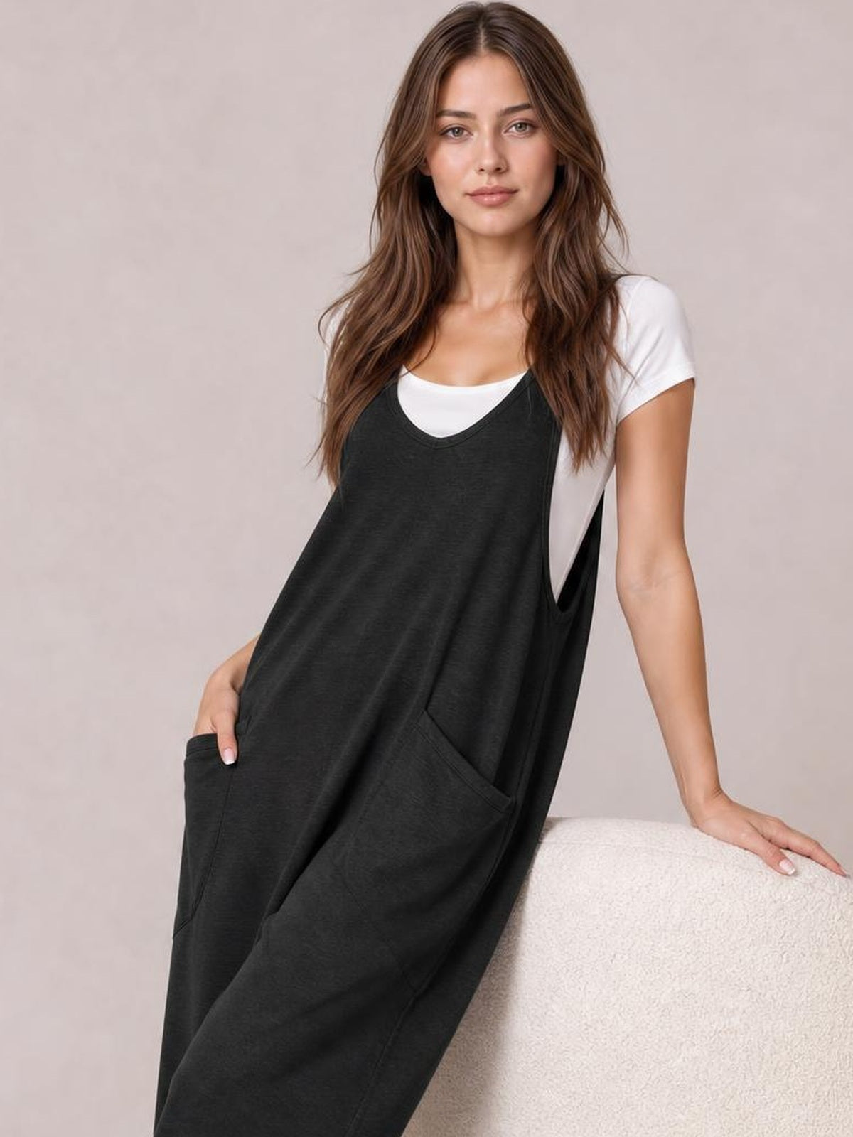 A model poses in a black wide-strap jumpsuit with a relaxed full-length silhouette, V-neckline, side cutouts, and large front patch pockets.