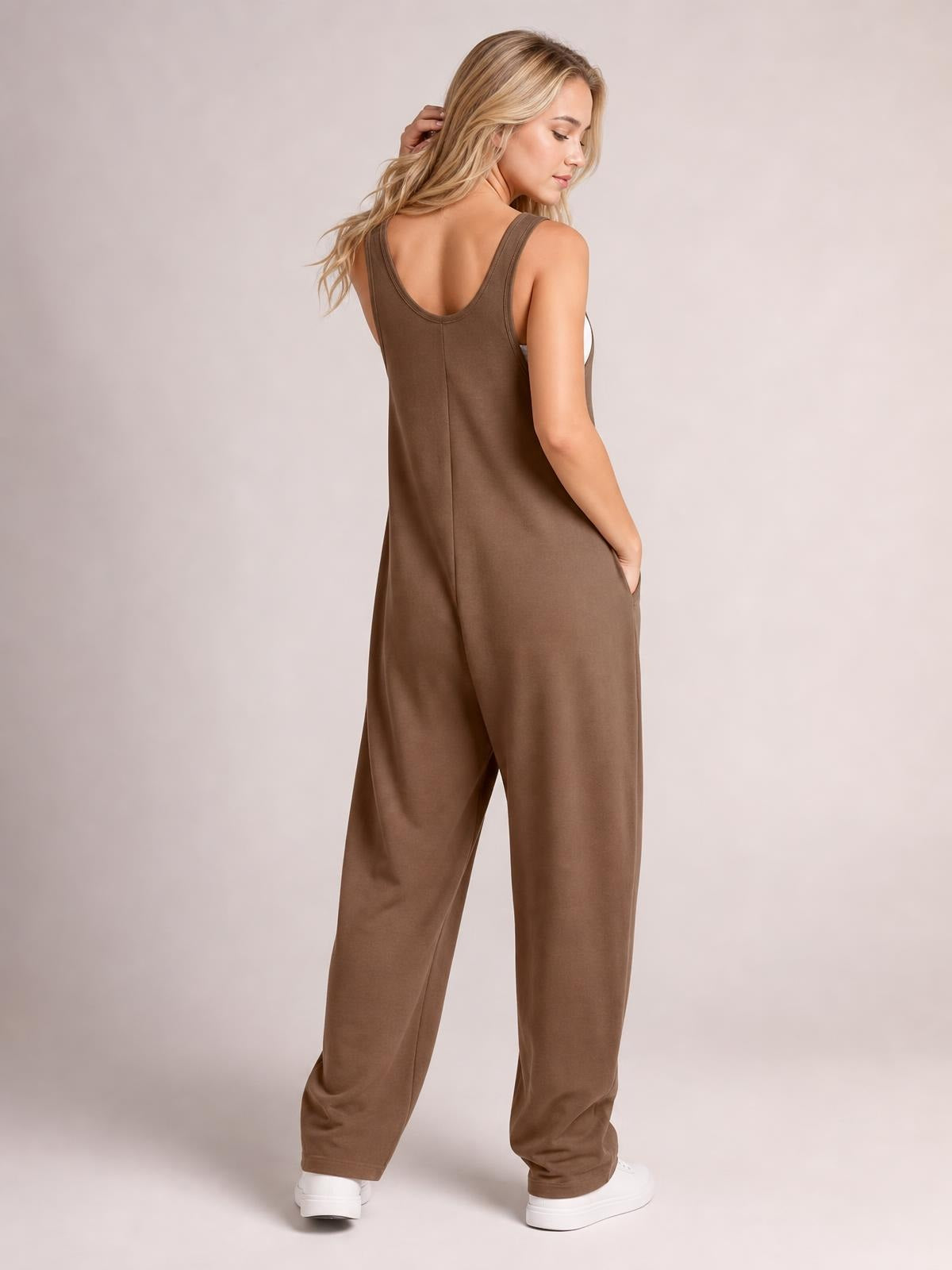 Model turns to show a brown wide-strap jumpsuit with a scoop back, relaxed wide-leg silhouette, center seam, and side pockets.