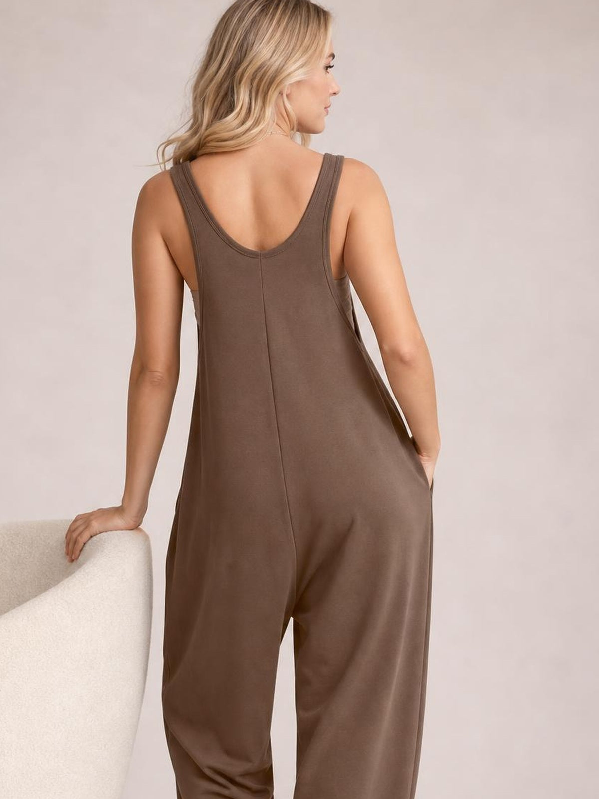 Model shown from the back wears a brown wide-strap jumpsuit with a scoop back, relaxed wide-leg silhouette, center seam, and side pockets.