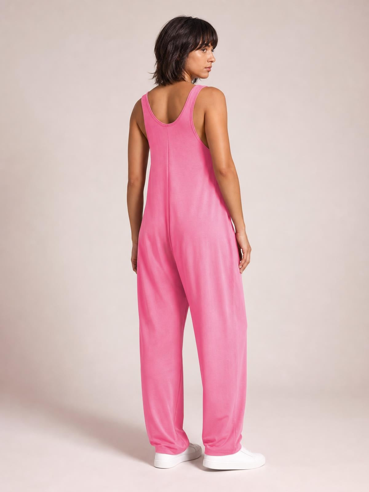 Model in a bright pink wide strap jumpsuit turns to show its scoop back, relaxed silhouette, straight wide legs, and practical side pockets.