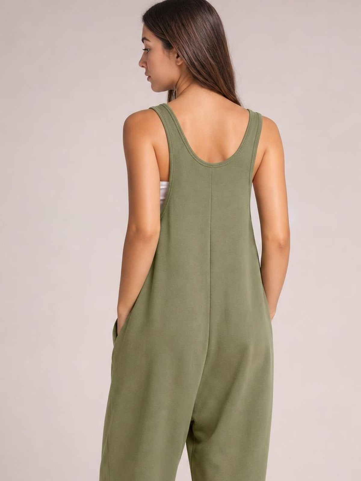 Model shown from the back wearing an olive green wide-strap jumpsuit with a relaxed, loose silhouette, low scoop back, and side pockets.