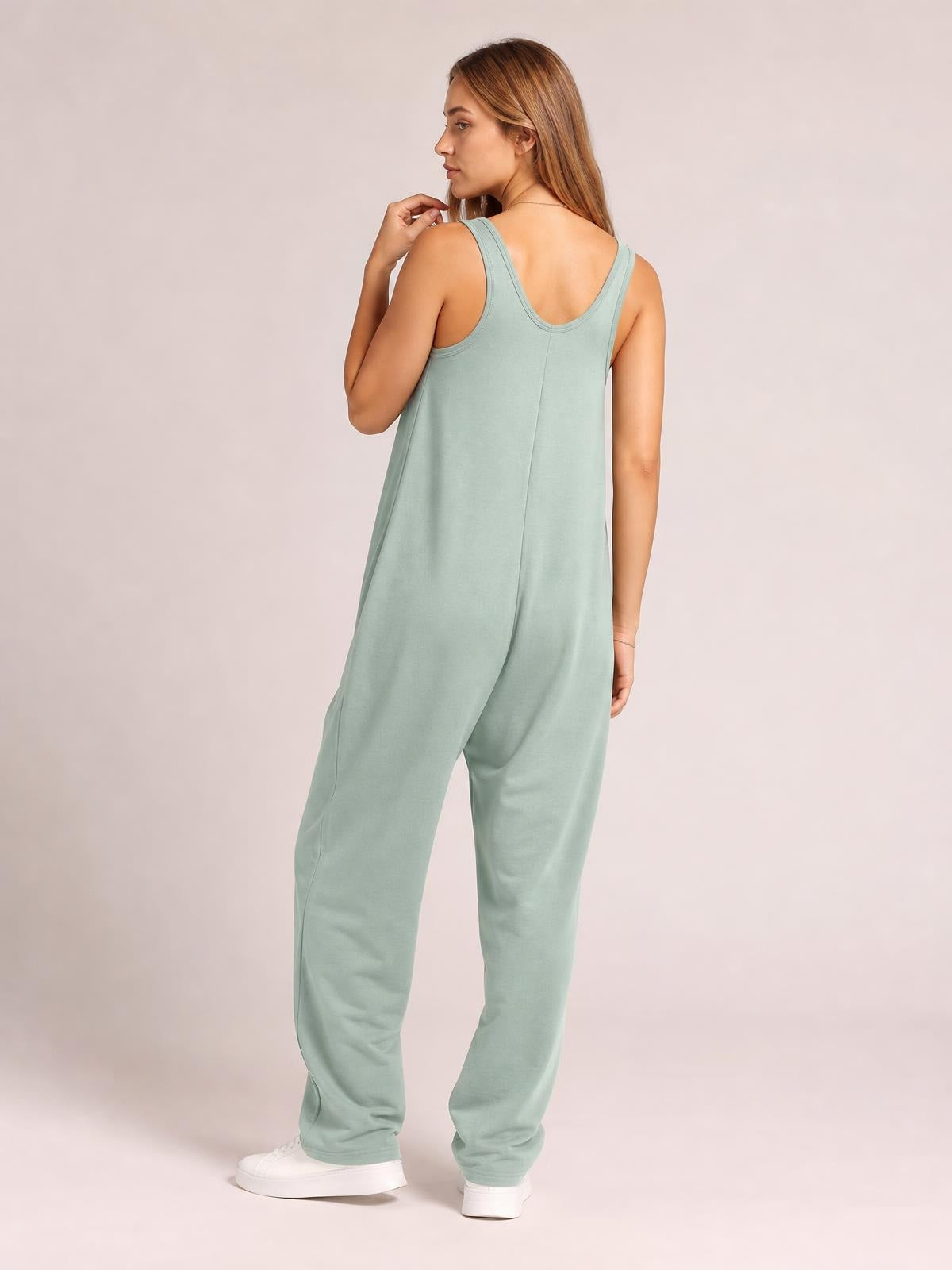 Model shown from the back in a sage green wide strap jumpsuit with a relaxed, wide-leg silhouette, scoop back, and side pockets.