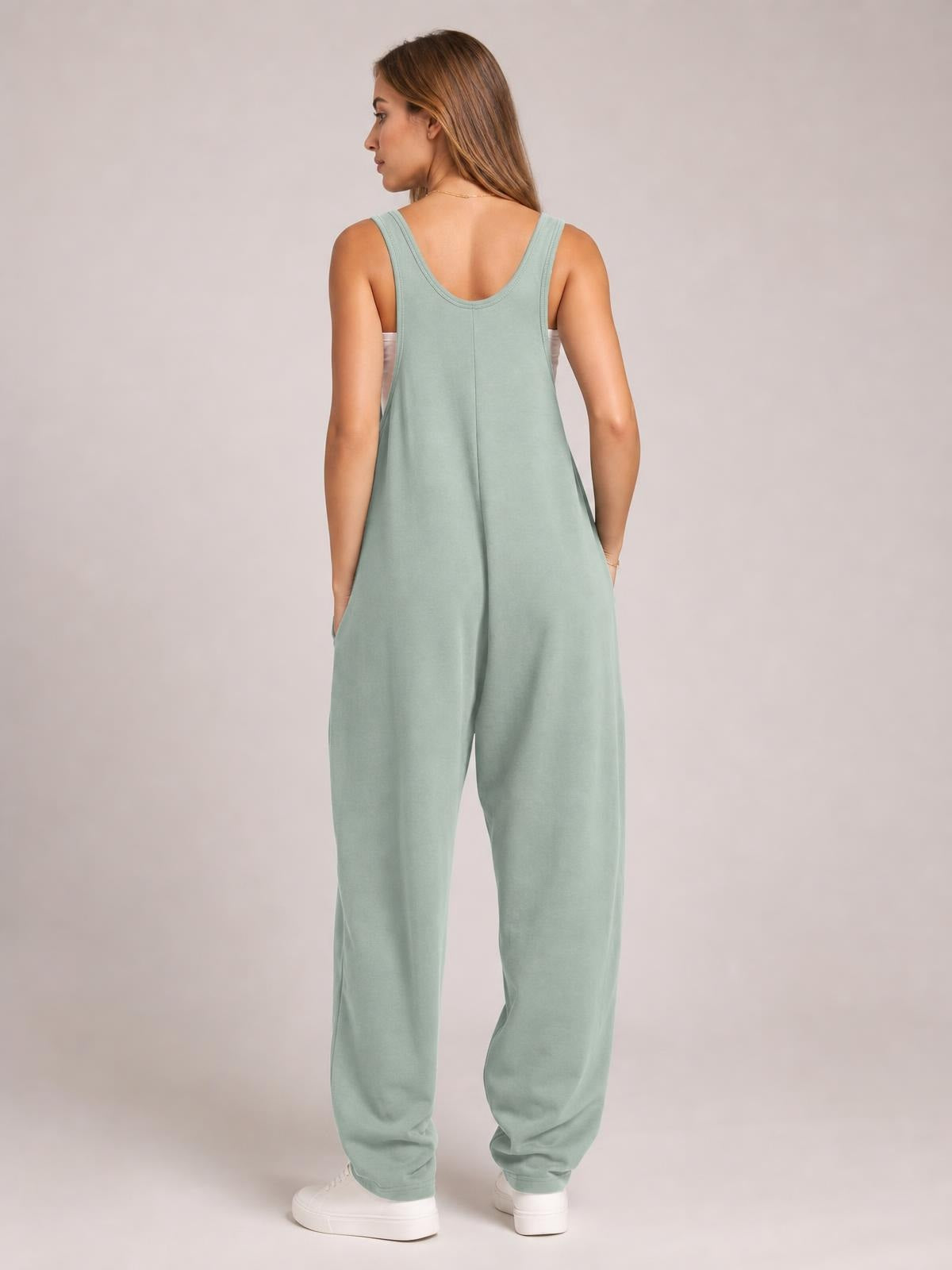Model shown from the back in a sage green wide-strap jumpsuit with a relaxed wide-leg silhouette, center seam, and side pockets.