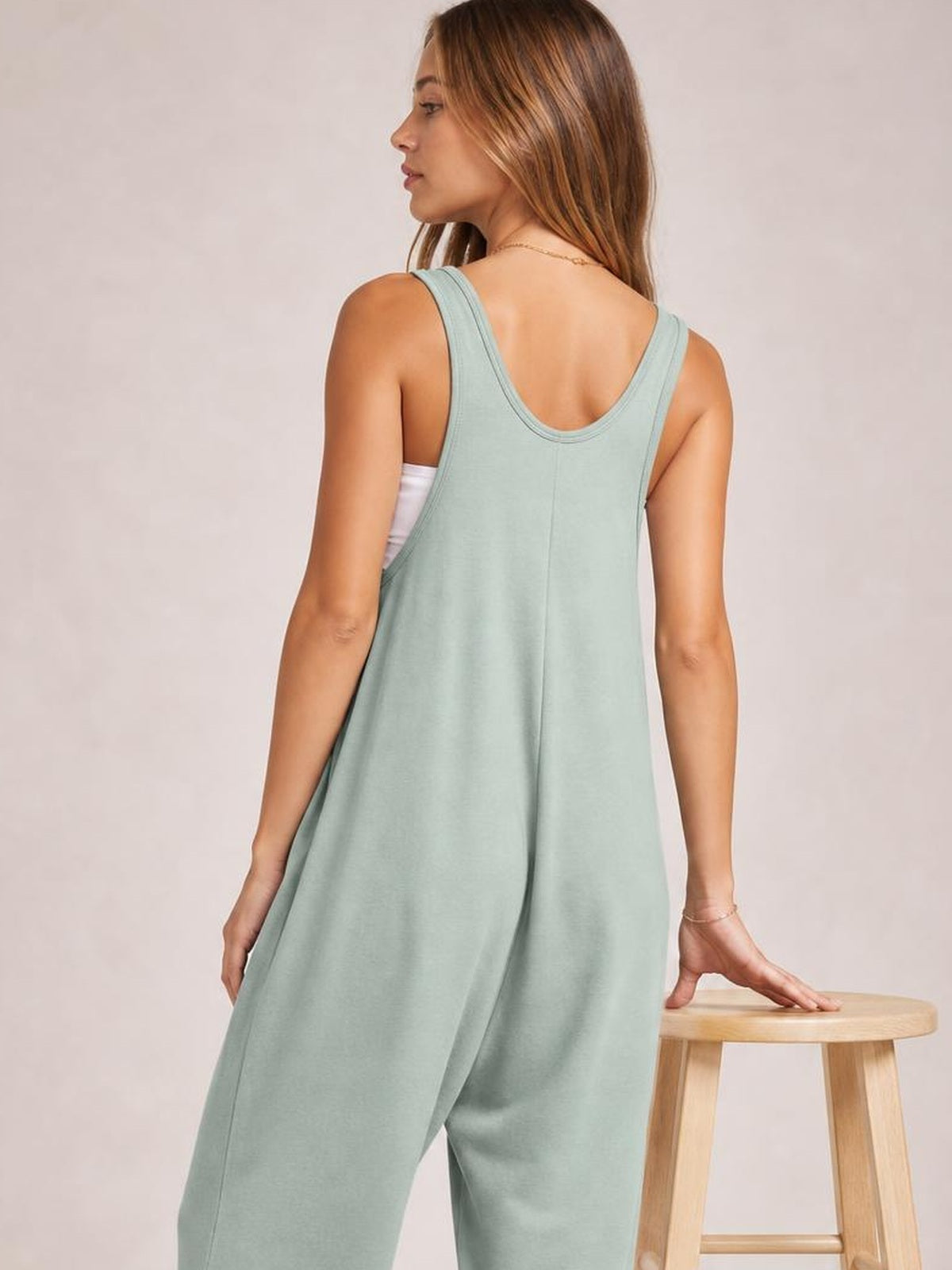 Model shown from the back in a sage green wide-strap jumpsuit with a scoop back, relaxed wide-leg silhouette, and side pockets.