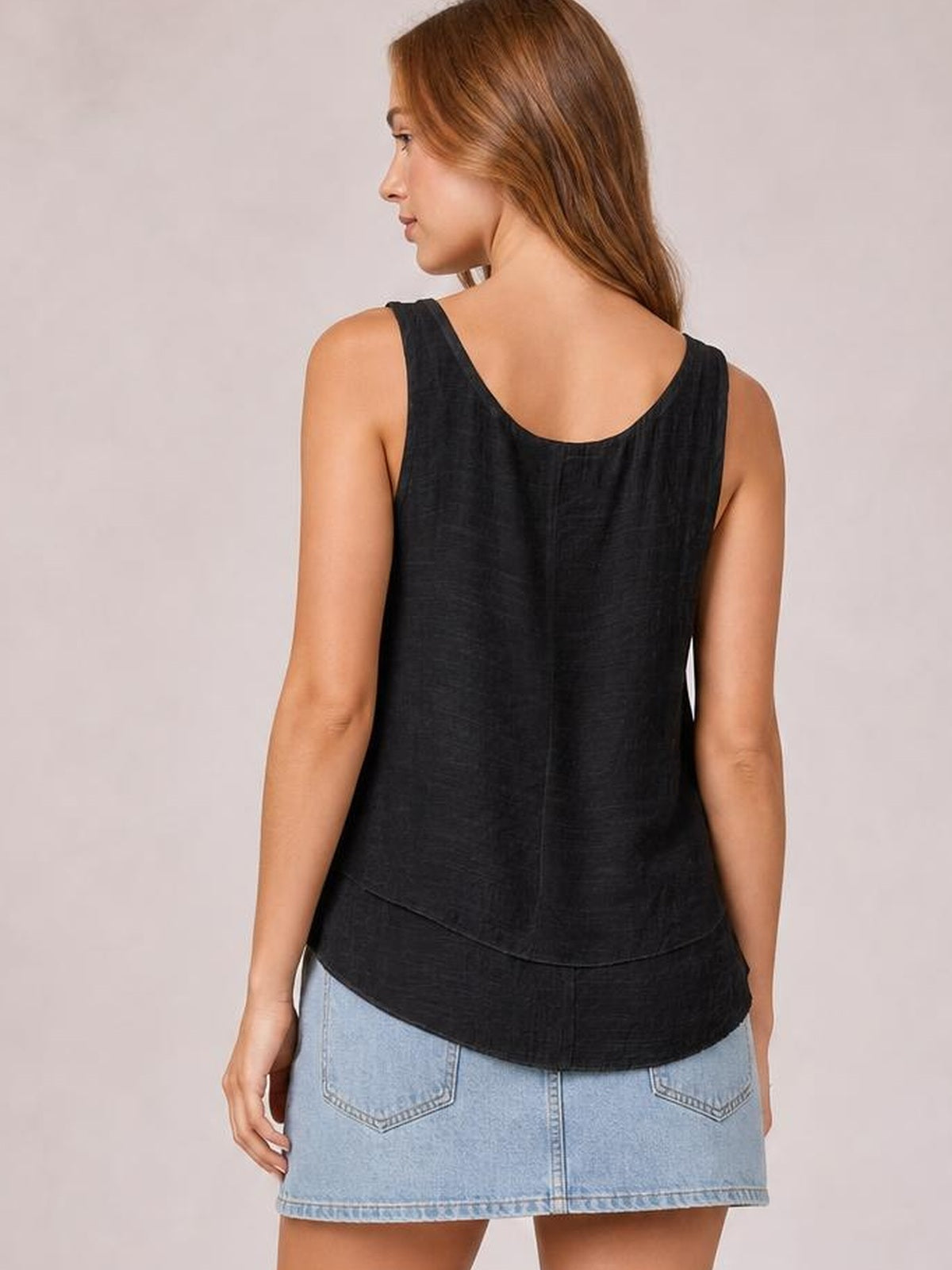 A model poses in profile wearing a black sheer layered tank with wide straps, a scoop back, relaxed straight silhouette, and curved hem.