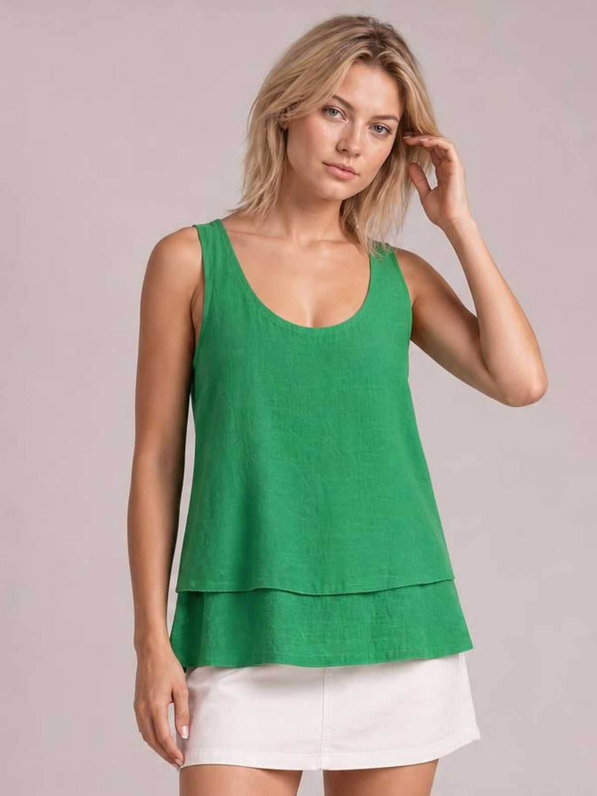A model poses in a green sheer layered tank with wide straps, a scoop neckline, relaxed silhouette, and tiered hem over white shorts.