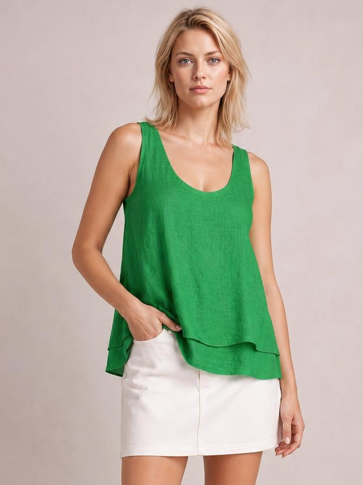 Model wearing a green sheer layered tank with wide straps, a scoop neckline, relaxed flowy silhouette, and overlapping curved hems, posing with one hand in her pocket.