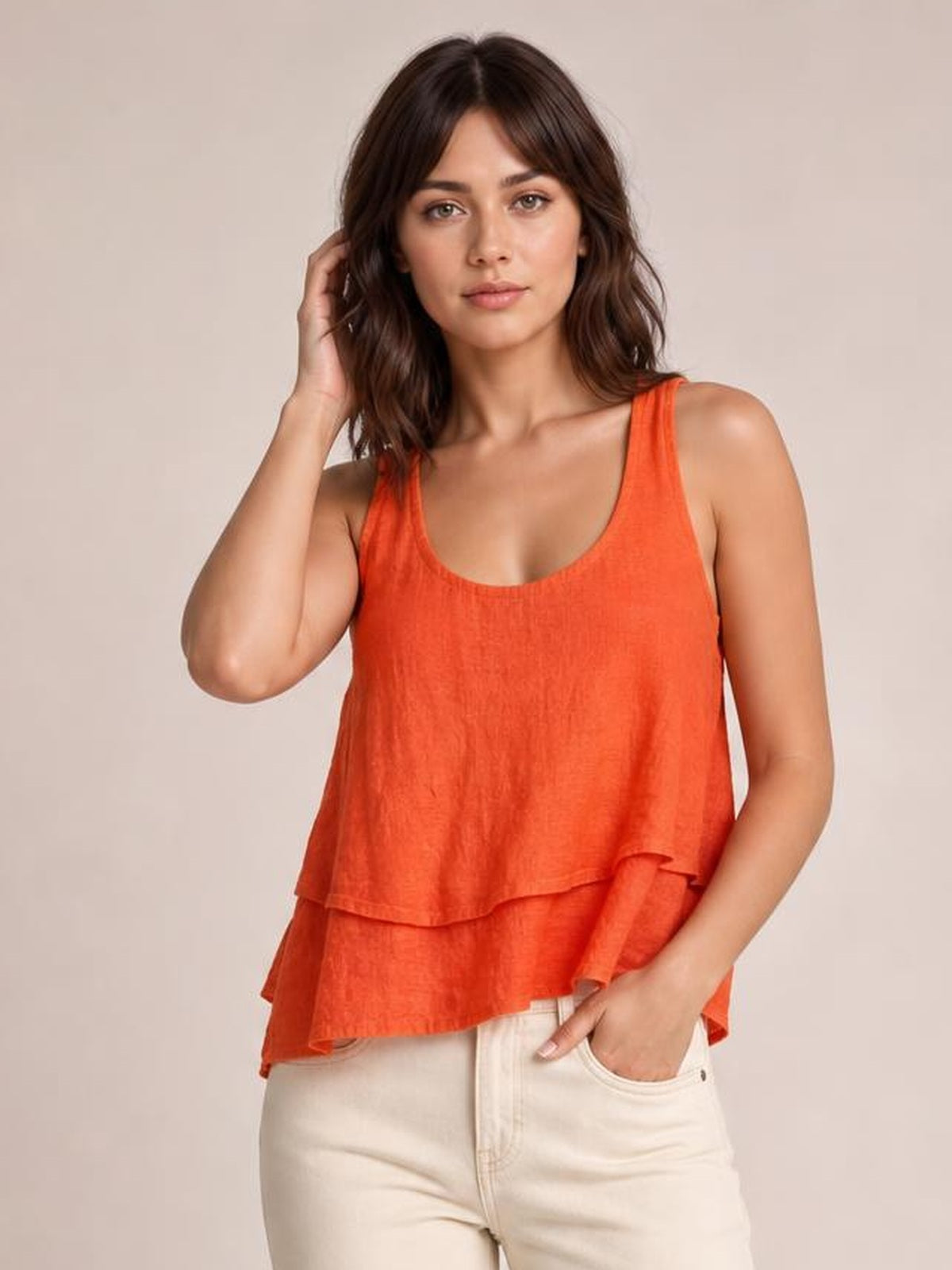 Model poses with one hand in her pocket wearing an orange sheer layered tank with wide straps, a scoop neckline, and a relaxed, tiered silhouette.