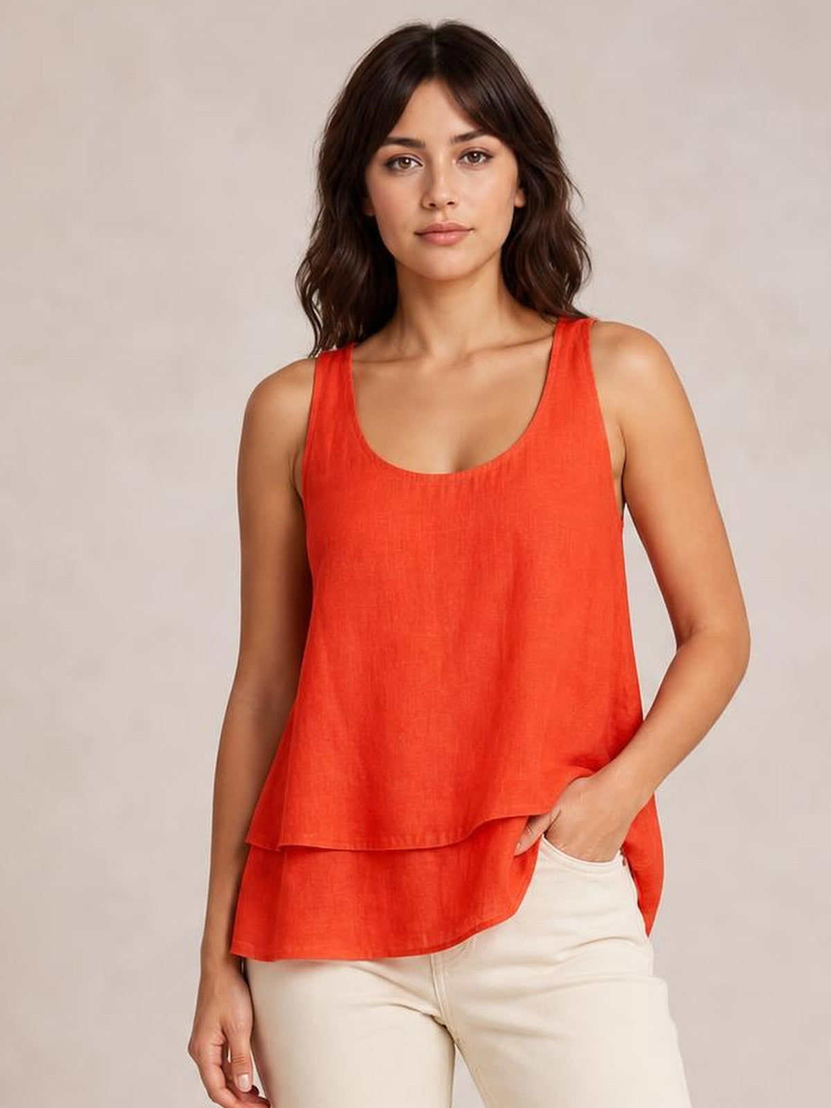 A model poses in a coral-red sheer layered tank with wide straps, a scoop neckline, and a loose, flowing two-tier silhouette.