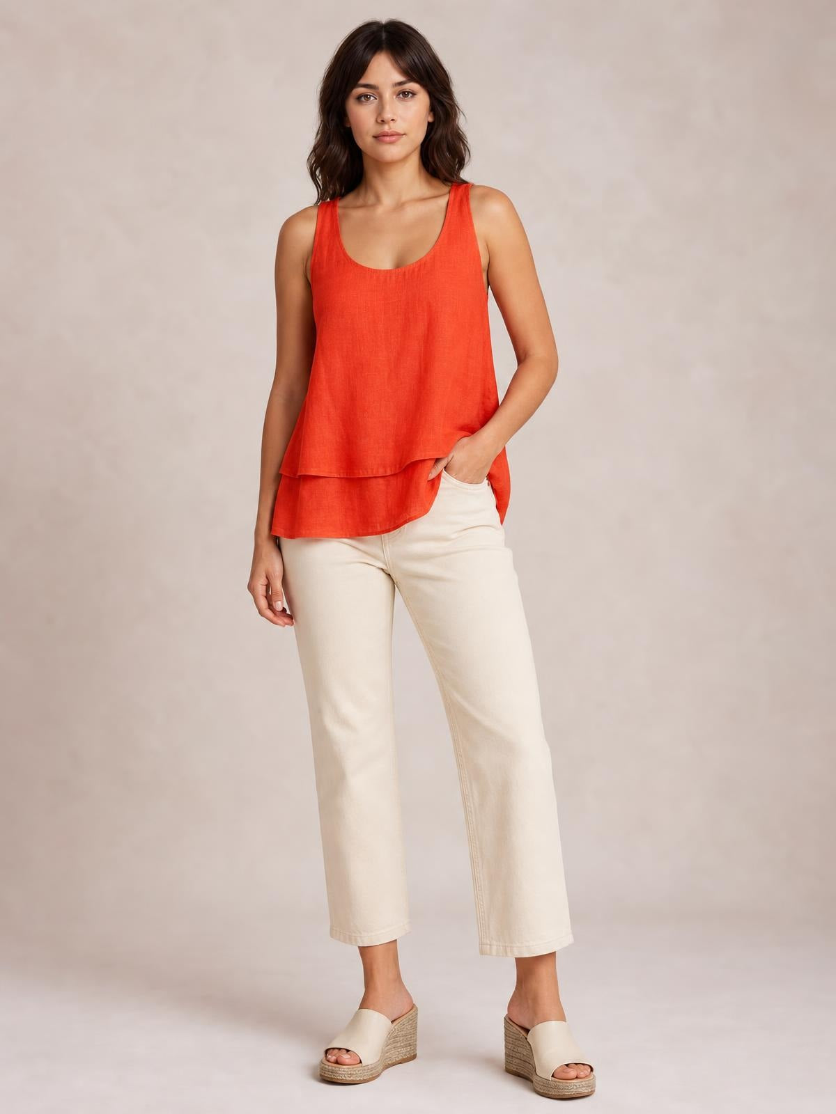 Model wearing a red wide-strap layered tank with a sheer, flowing tiered silhouette and scoop neckline, posed with one hand in her pocket.