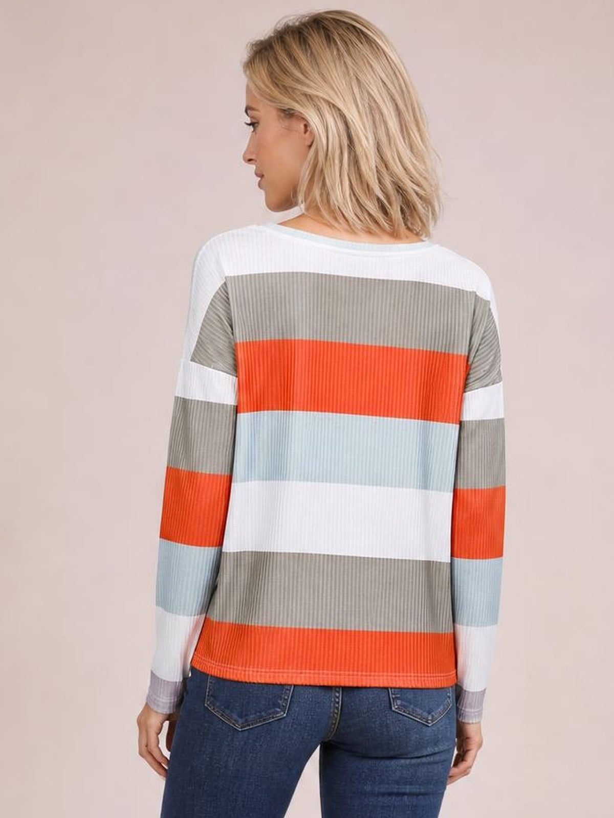 Model shown from the back wearing a long-sleeve wide stripe top with bold horizontal bands in white, gray, coral, and light blue, with a relaxed silhouette.