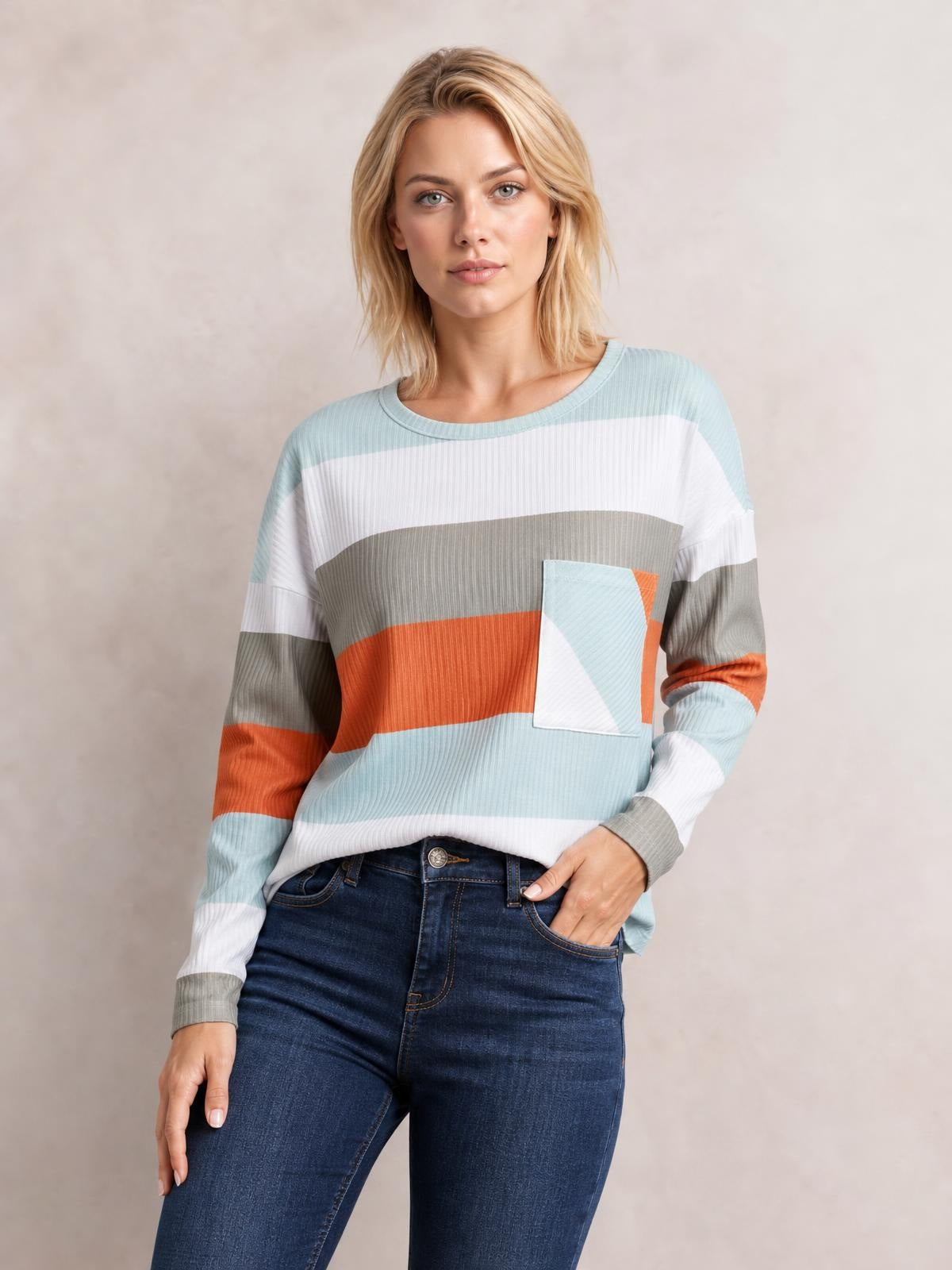 A model poses in a relaxed wide stripe top with long sleeves, a crew neckline, ribbed texture, multicolor horizontal bands, and a chest pocket.