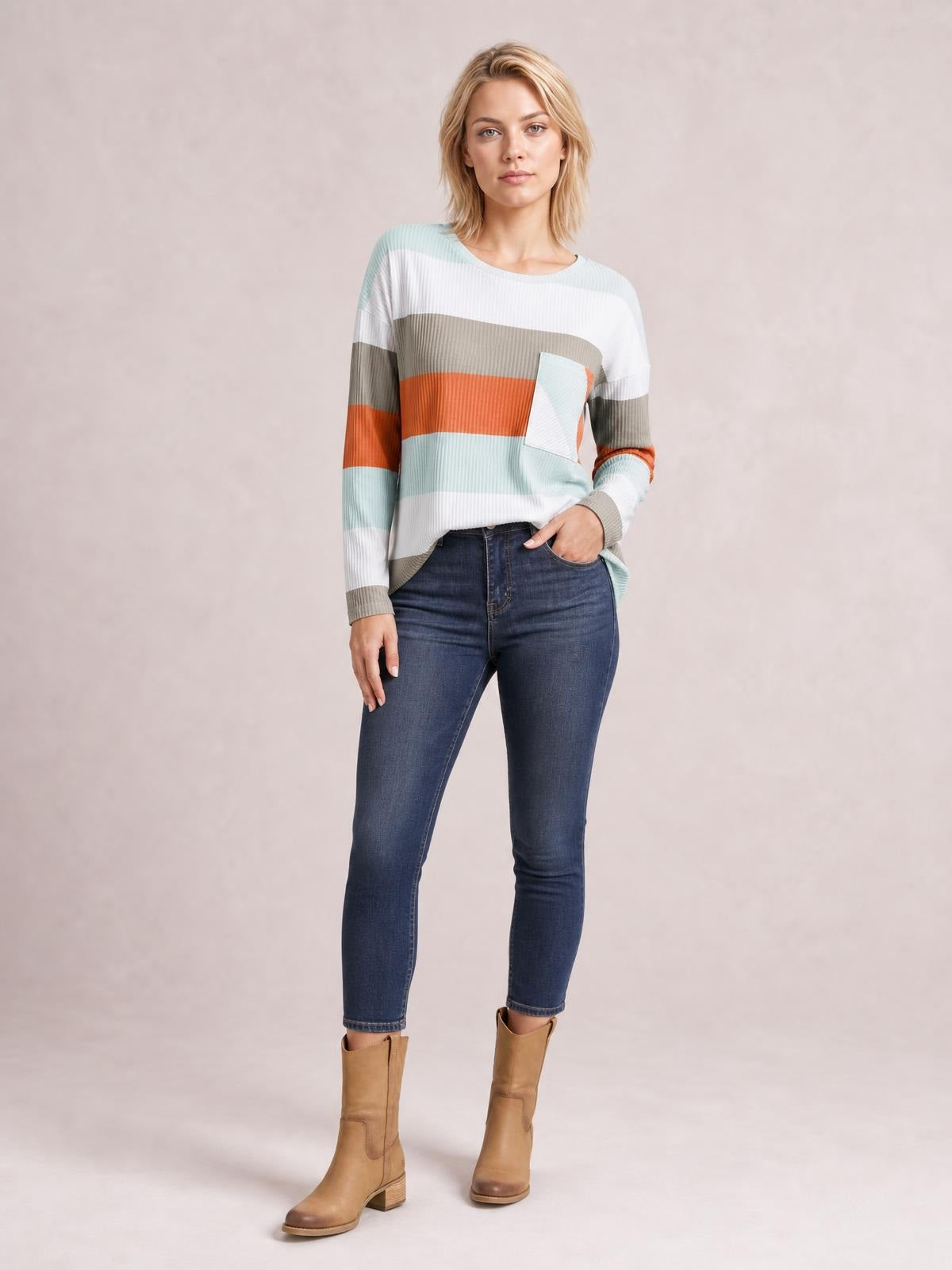 Model wears an opaque wide stripe top with a chest pocket, crew neckline, long sleeves, ribbed cuffs, and a relaxed silhouette while standing with one hand in her jeans pocket.