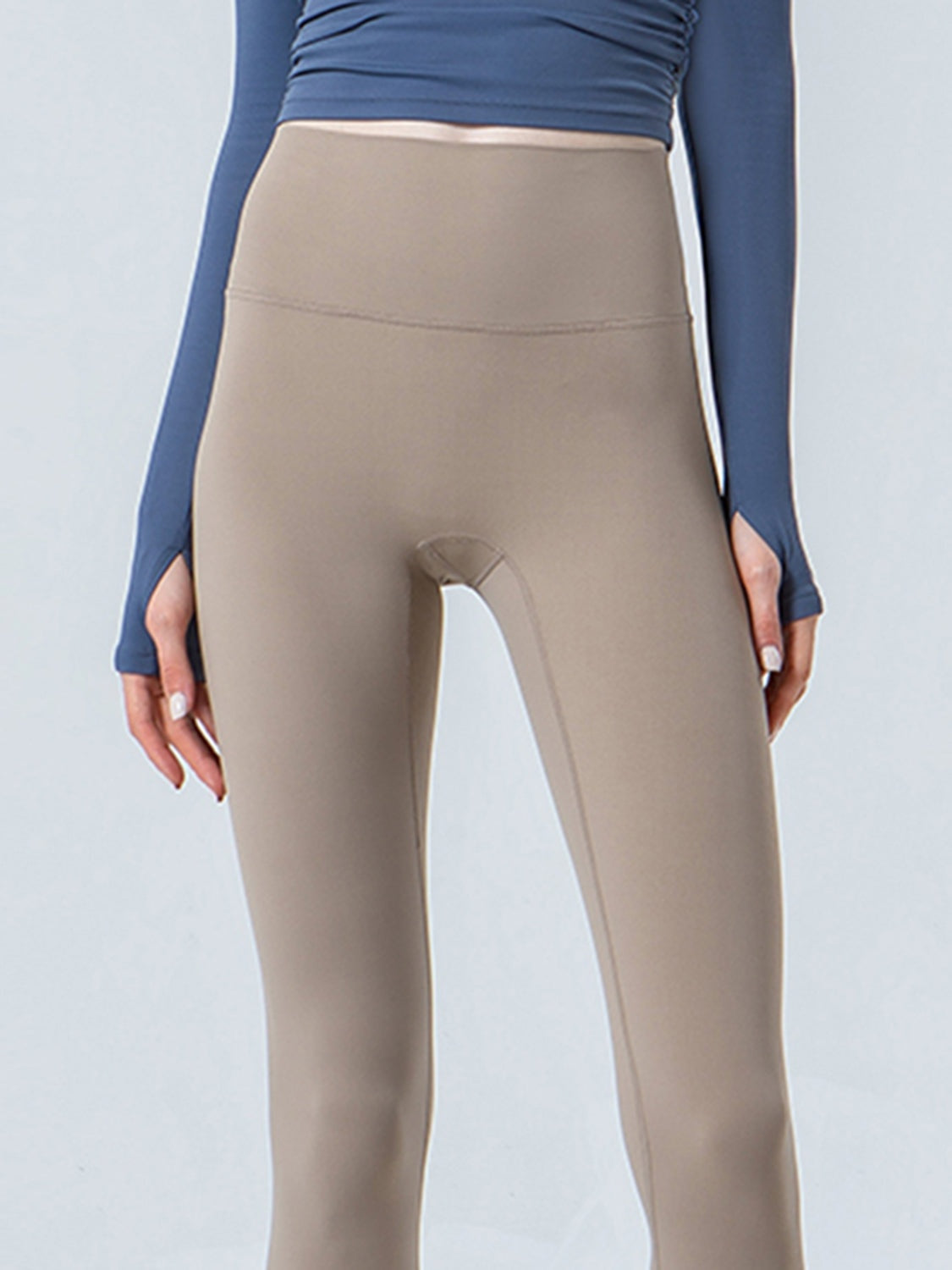 A model stands with hands at her sides wearing taupe wide-waistband sports leggings with a smooth, stretchy fitted silhouette and visible panel seam.