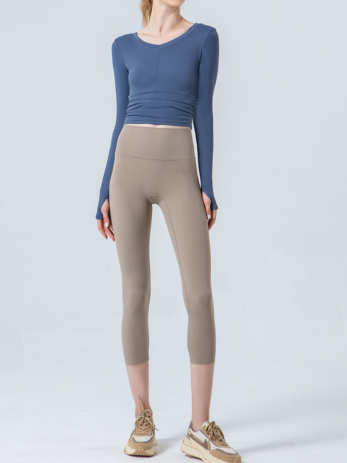 A model stands in taupe cropped sports leggings with a wide waistband, smooth construction, and a close-fitting silhouette ending at mid-calf.