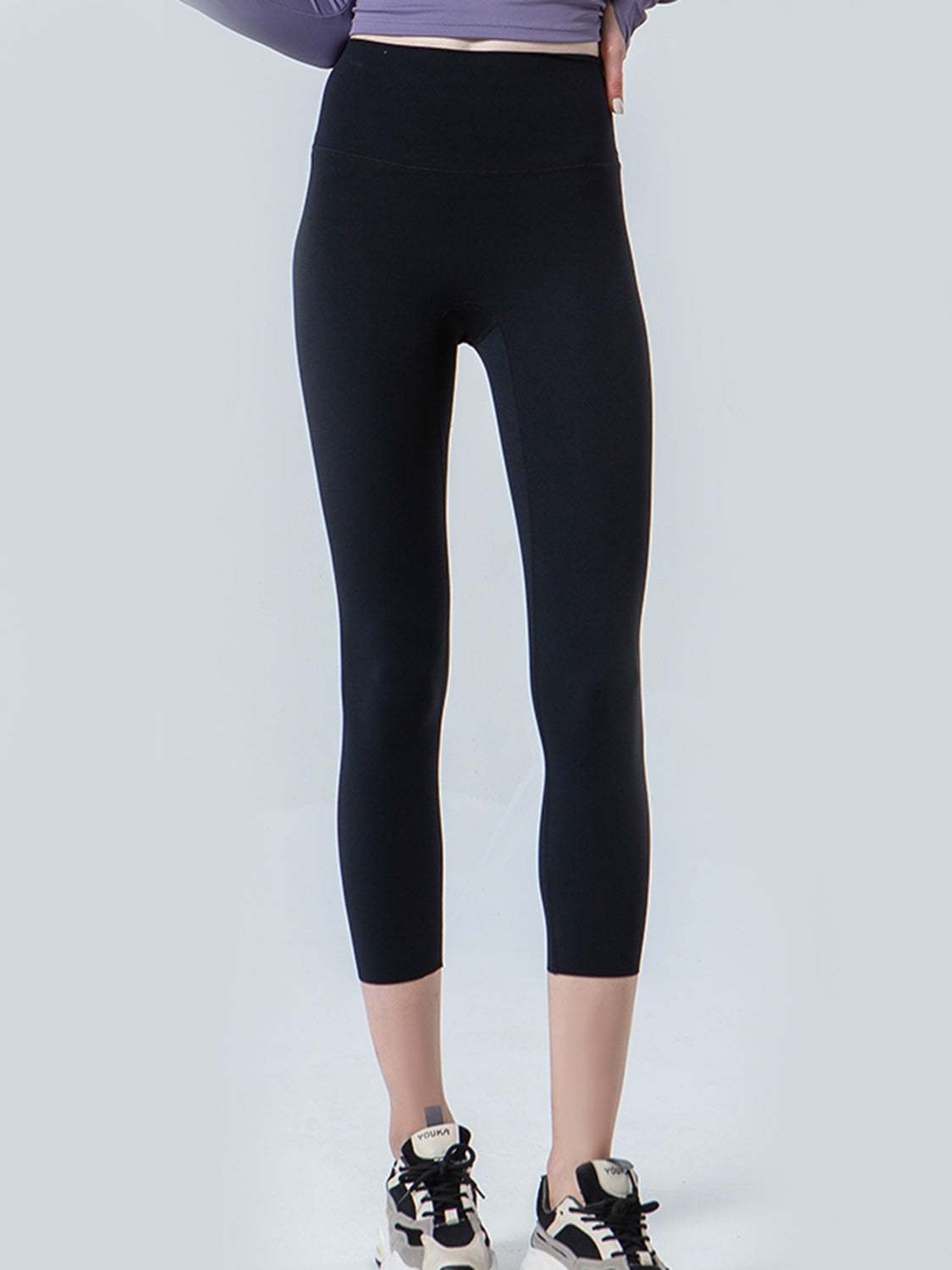 A model stands in black cropped sports leggings with a wide waistband, smooth opaque construction, and a close-fitting silhouette ending mid-calf.