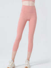 A model stands with one leg slightly bent in pink cropped sports leggings featuring a wide waistband, fitted silhouette, and visible front seam construction.