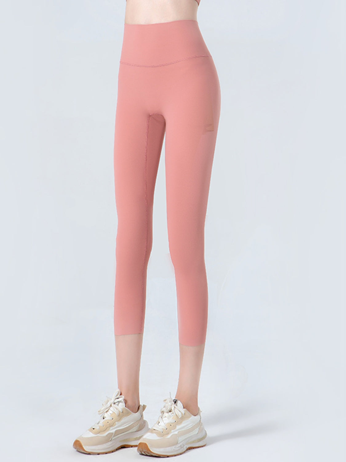 Model wears coral cropped sports leggings with a wide waistband, high-rise fit, visible seams, and a close, stretchy silhouette ending mid-calf.