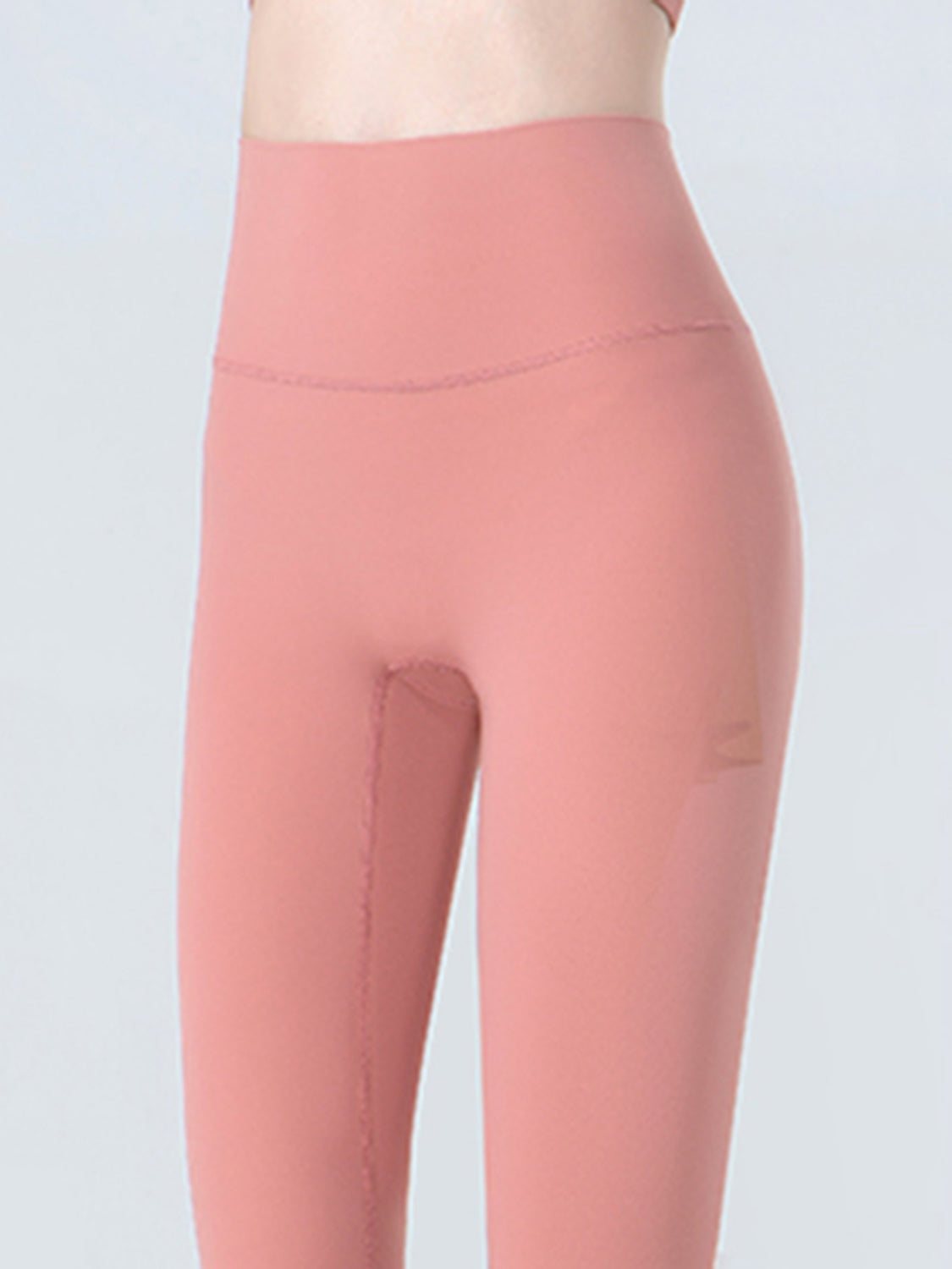 A model wears coral pink cropped sports leggings with a wide waistband and smooth, close-fitting stretchy silhouette in a front-facing close-up.
