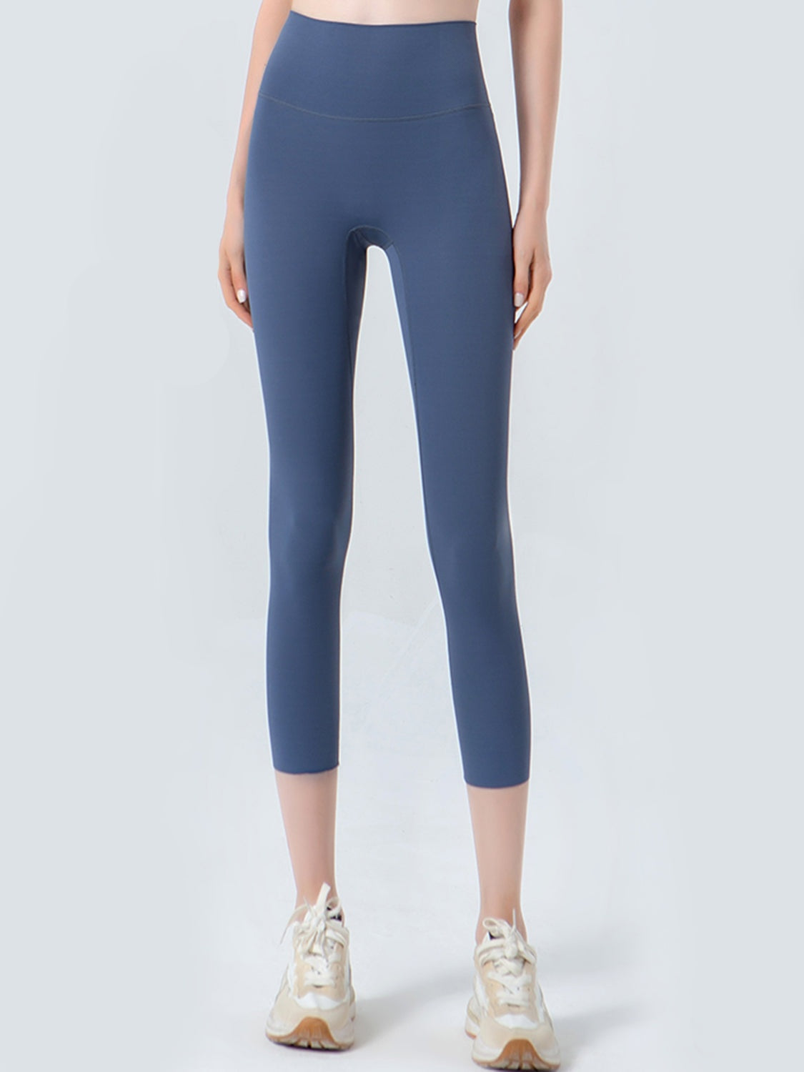 Model stands facing forward in navy cropped sports leggings with a wide high waistband, smooth opaque construction, and a close-fitting ankle-length silhouette.