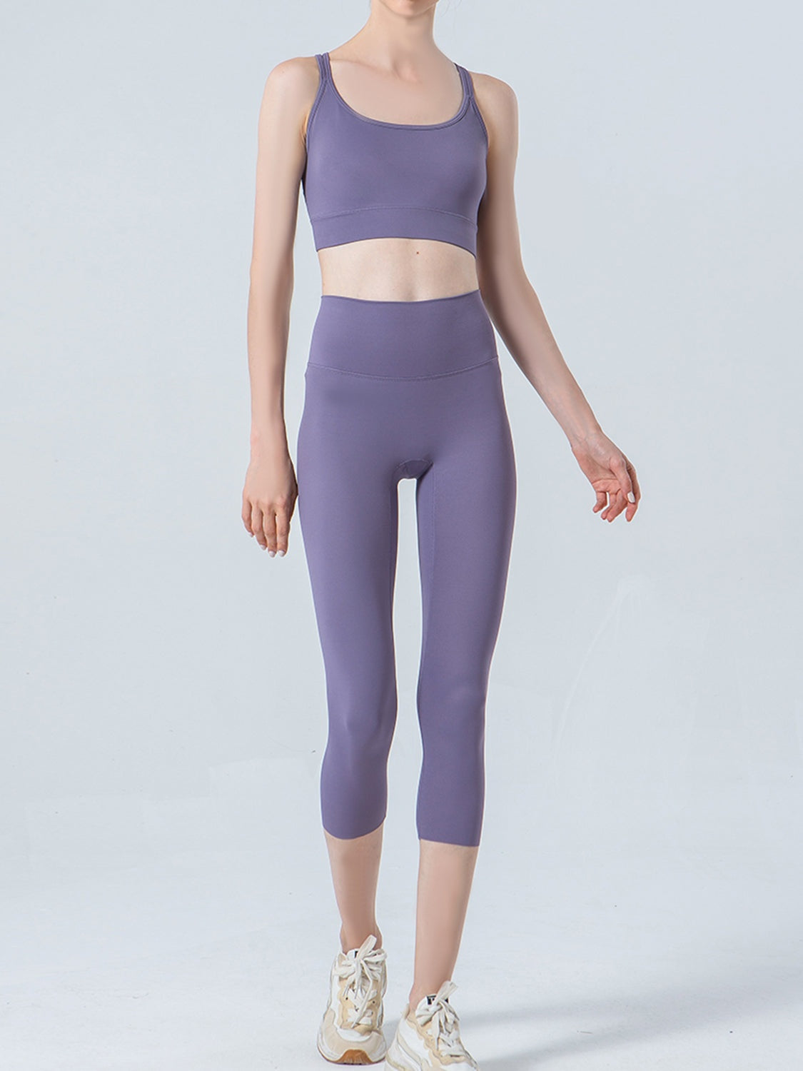 Model in a relaxed standing pose wears lavender-purple cropped sports leggings with a wide waistband, smooth opaque fabric, and a close-fitting ankle-length silhouette.