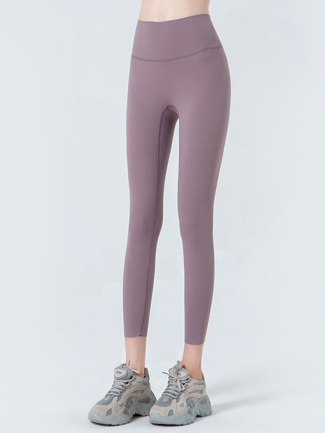 Model standing in mauve cropped sports leggings with a wide waistband, high-rise silhouette, opaque stretch fabric, and visible curved and leg seams.