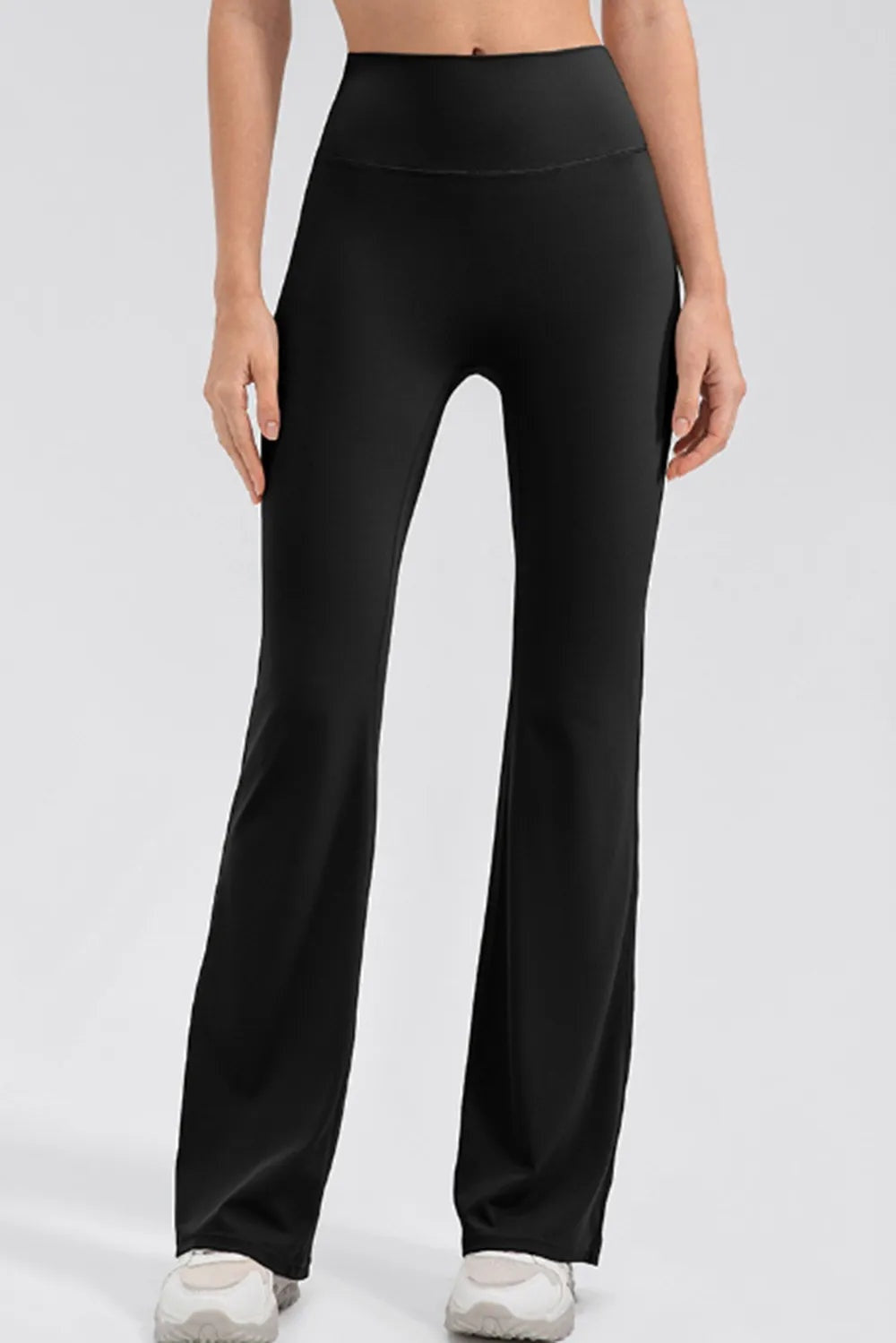 Model standing in black high-waist bootcut active leggings with a wide waistband, smooth fitted silhouette through the hips, and gently flared hems.