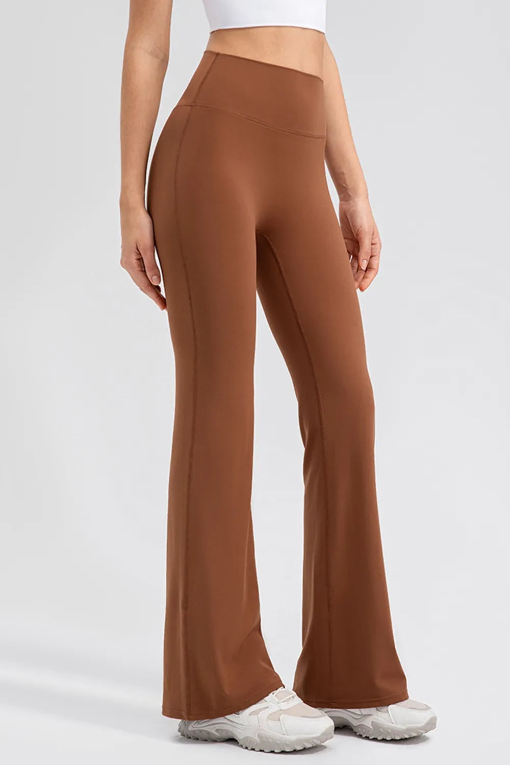 Model standing in brown high-waist bootcut active leggings with a wide waistband, fitted silhouette, and visible seam construction.