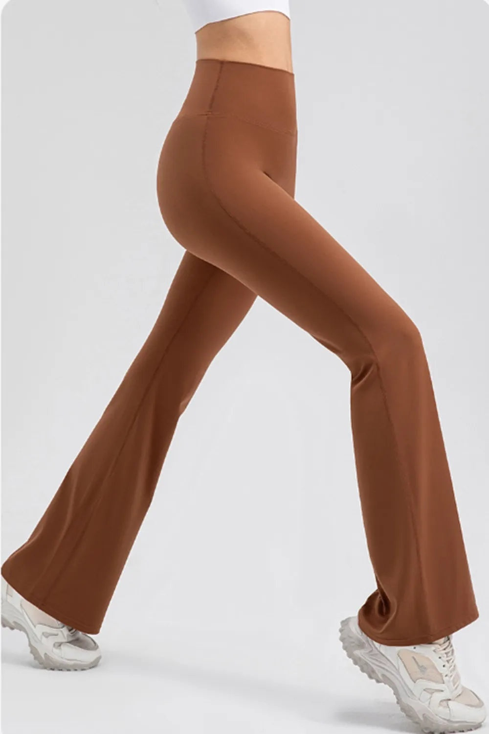 Model crosses one leg forward to showcase brown high-waisted bootcut active leggings with a wide waistband and smooth, stretchy construction.