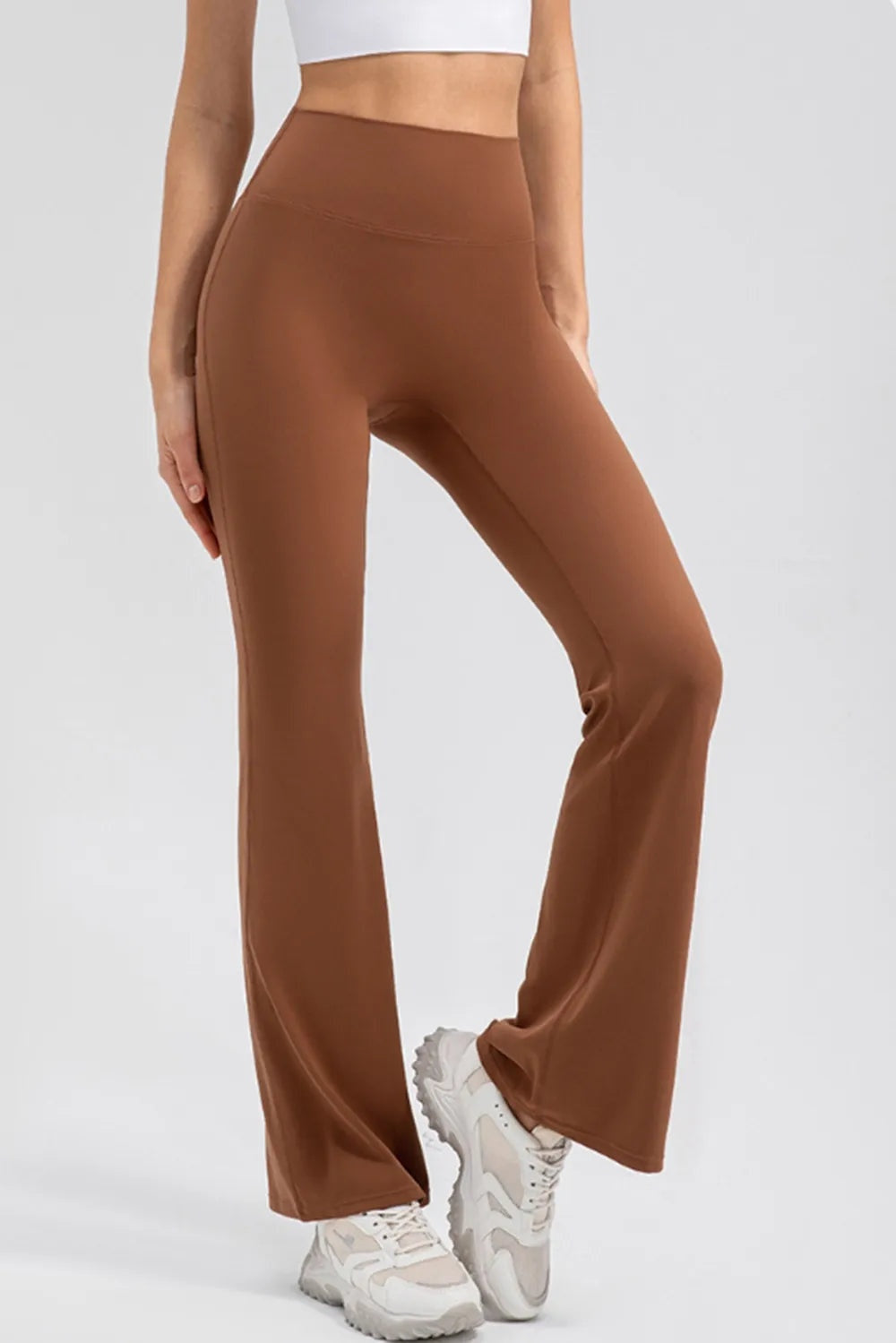 A model poses in brown high-waist active leggings with a wide waistband, smooth stretch construction, and a fitted bootcut silhouette.