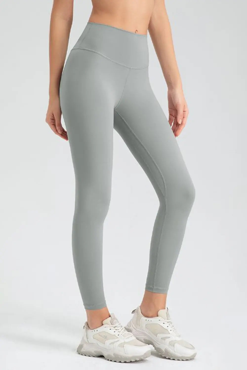 Model wearing light gray wide-waistband slim-fit active leggings with a high-rise silhouette, curved waistband seam, and fitted ankle-length construction.