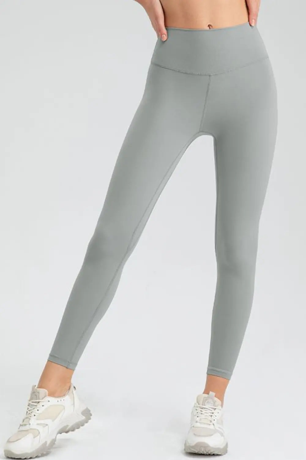 Model wearing gray wide-waistband slim-fit active leggings with a high-rise silhouette, visible seam construction, and tapered full-length legs.